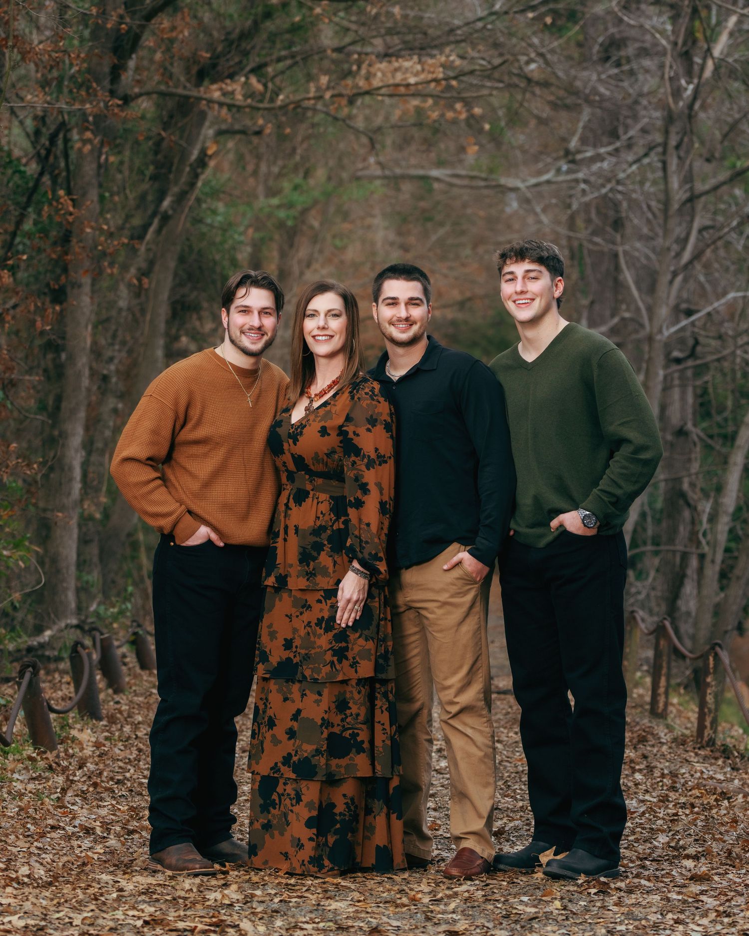 A family of four poses together on a wooded autumn path with fall foliage.