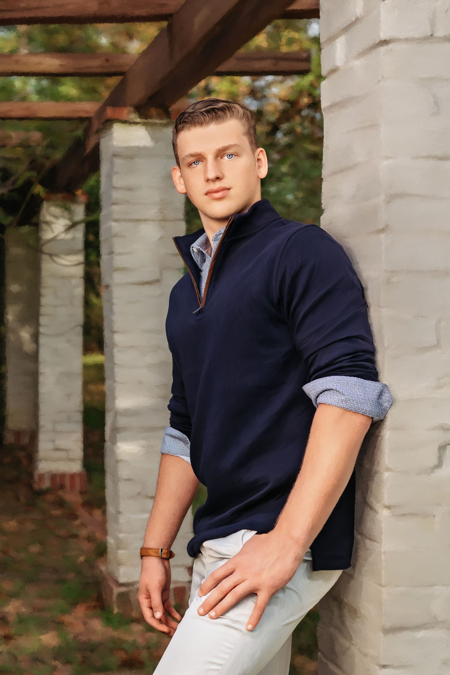 Young man in navy zip-up sweater and white pants leaning against stone pillar outdoors.