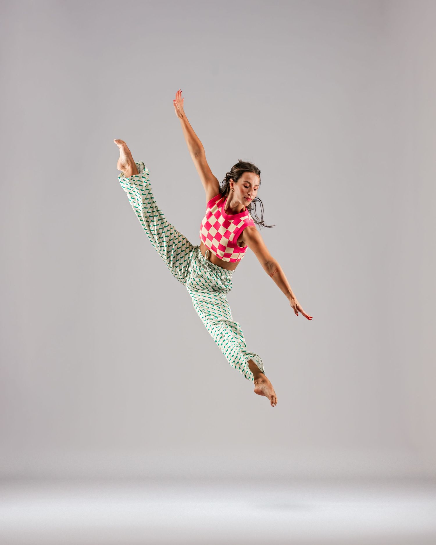 Dynamic dancer leaps mid-air wearing colorful checkered outfit against neutral studio background.