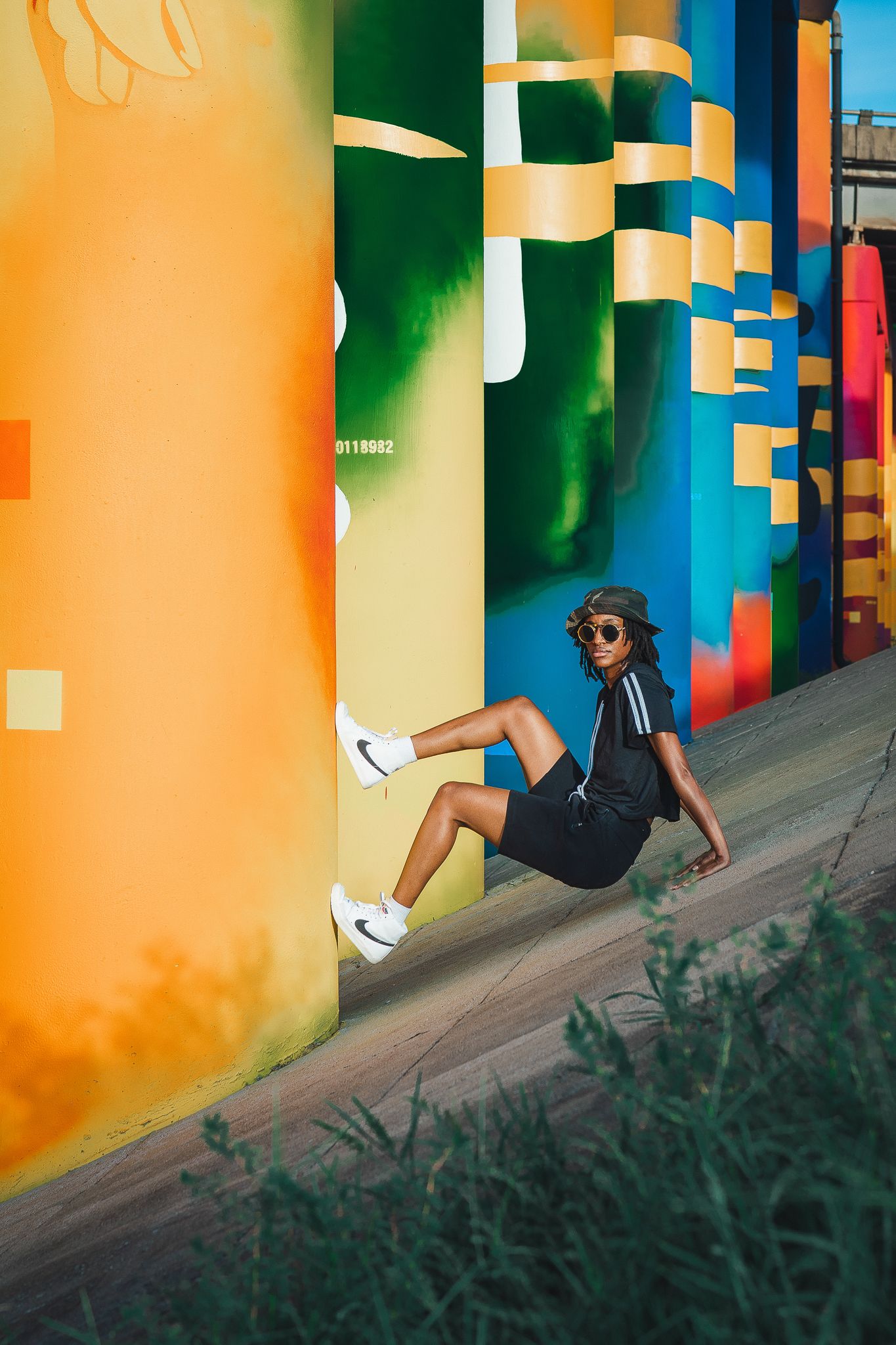 Person in black outfit leaning against vibrant colorful mural columns outdoors.