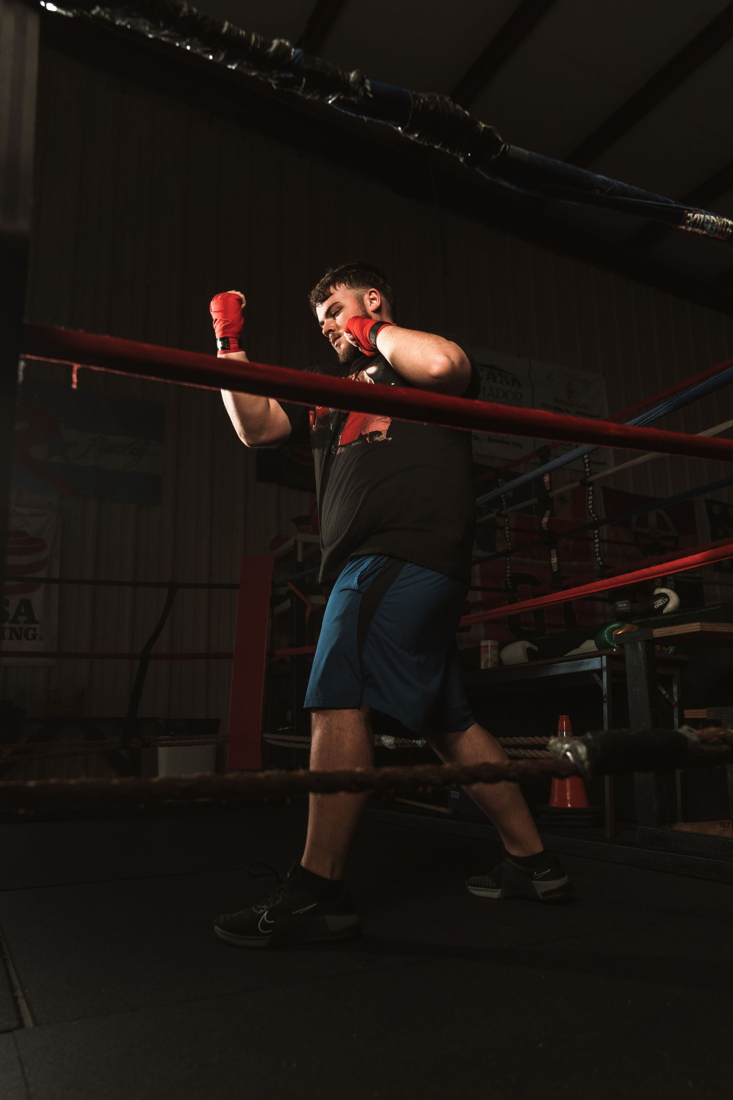 Male boxer in red gloves throwing punch in dark boxing ring gym.