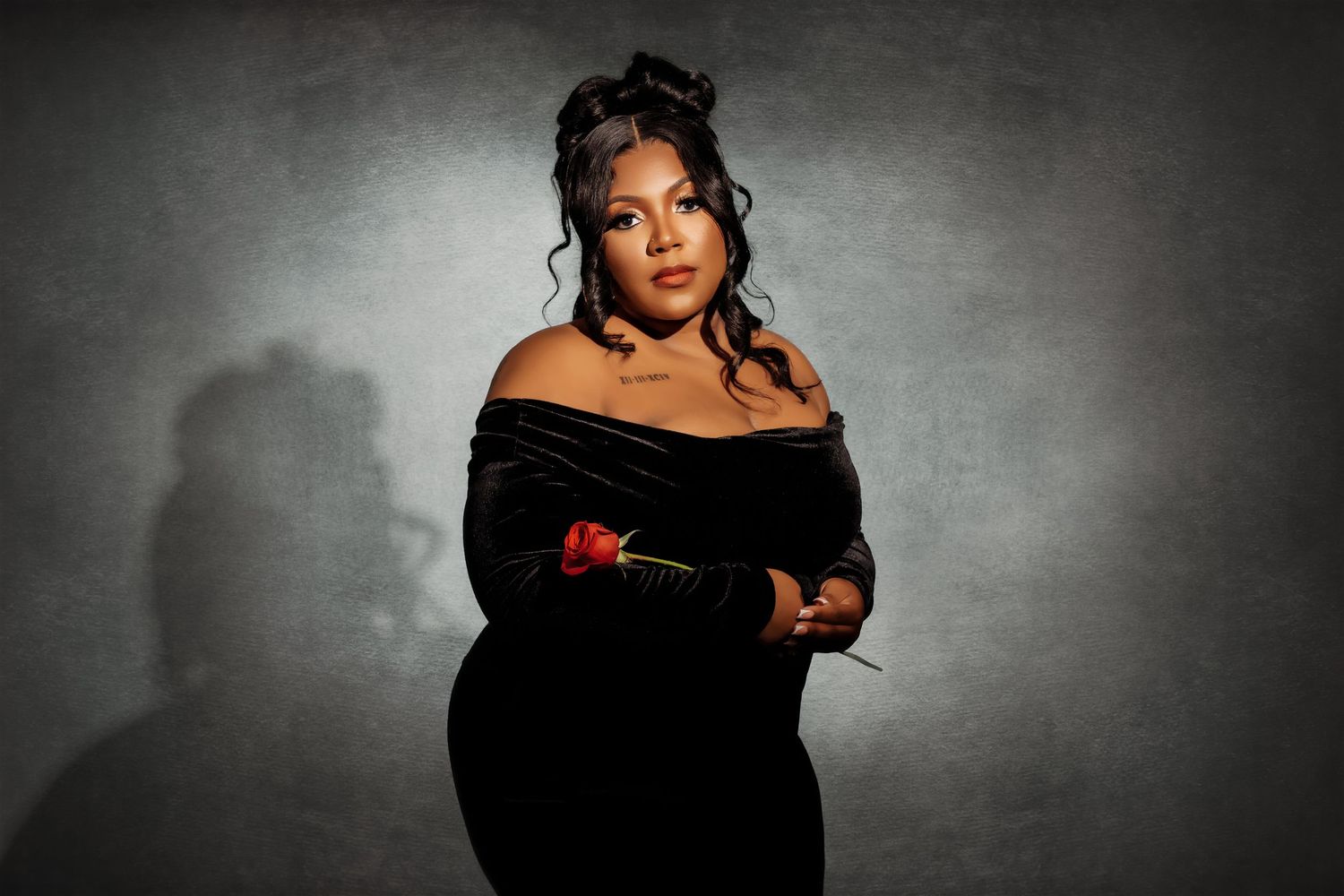 Plus-size woman in black off-shoulder velvet gown holding red rose in studio.