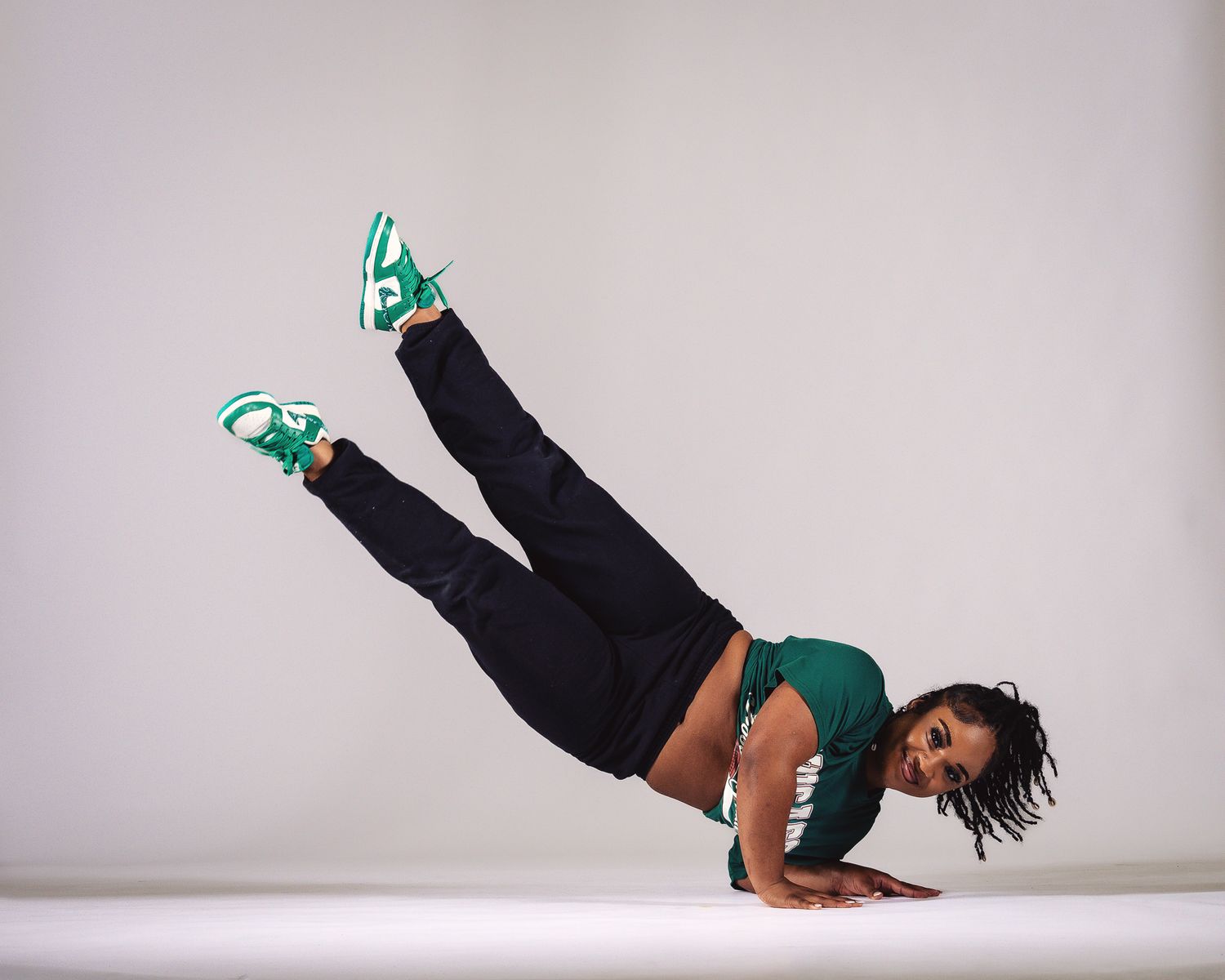 Athletic dancer performs impressive one-arm balance move wearing green sneakers and black outfit.