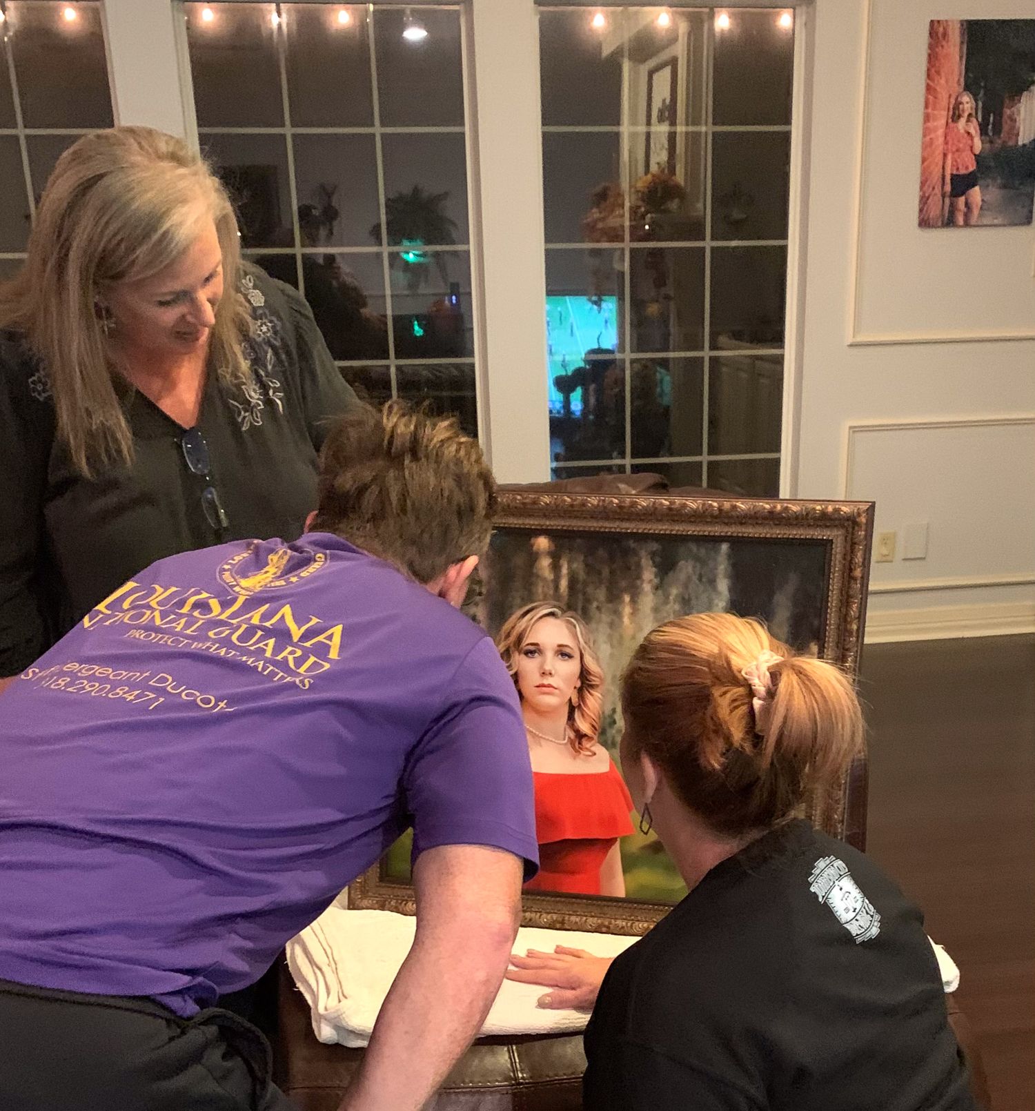People examining a framed portrait painting of a woman in red dress at an indoor art event.