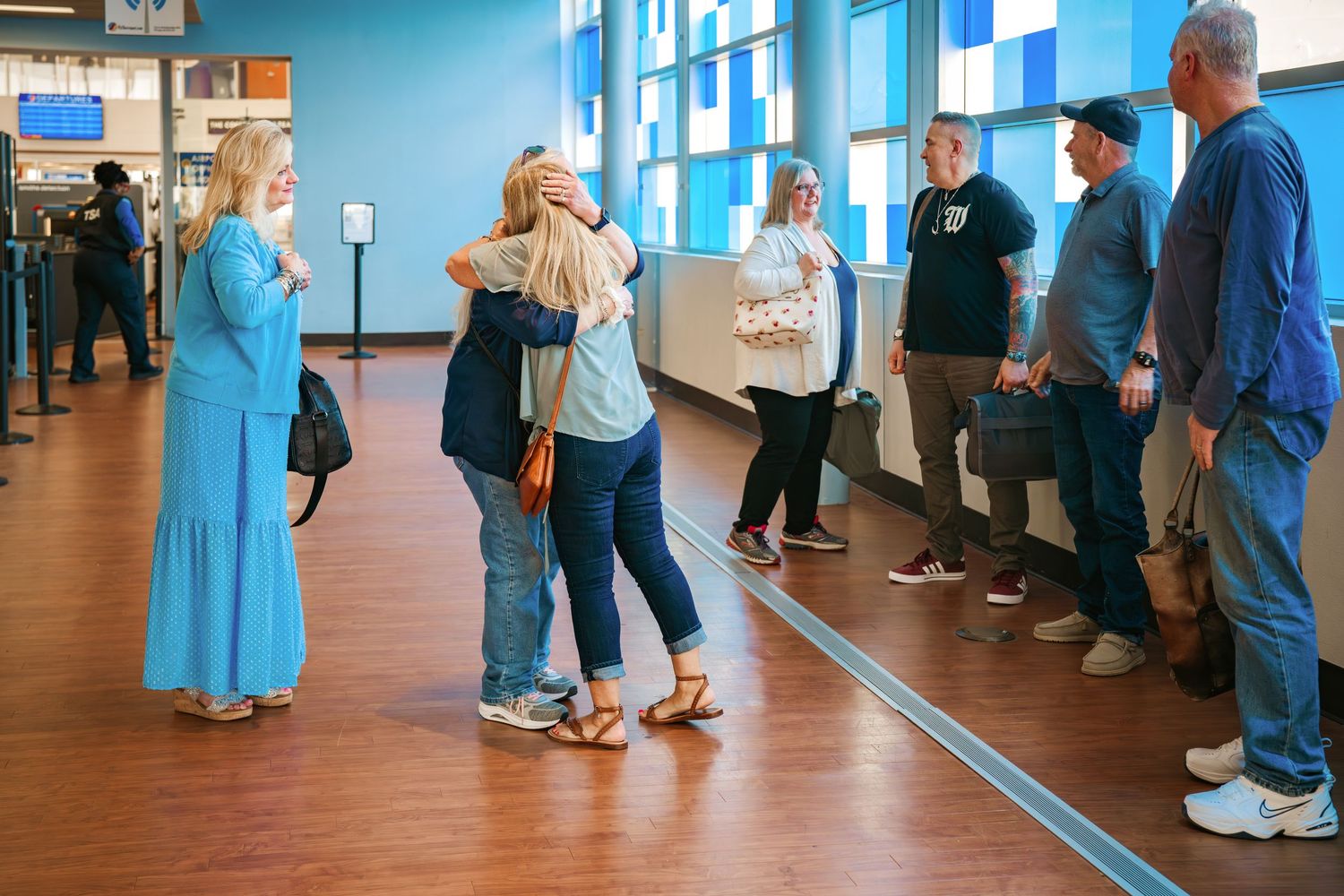 Group of people hugging and greeting each other in a colorful airport terminal.