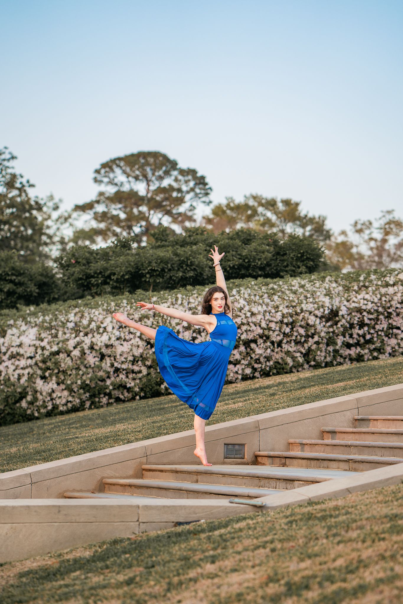 Graceful dancer performs arabesque in blue dress on outdoor garden steps.