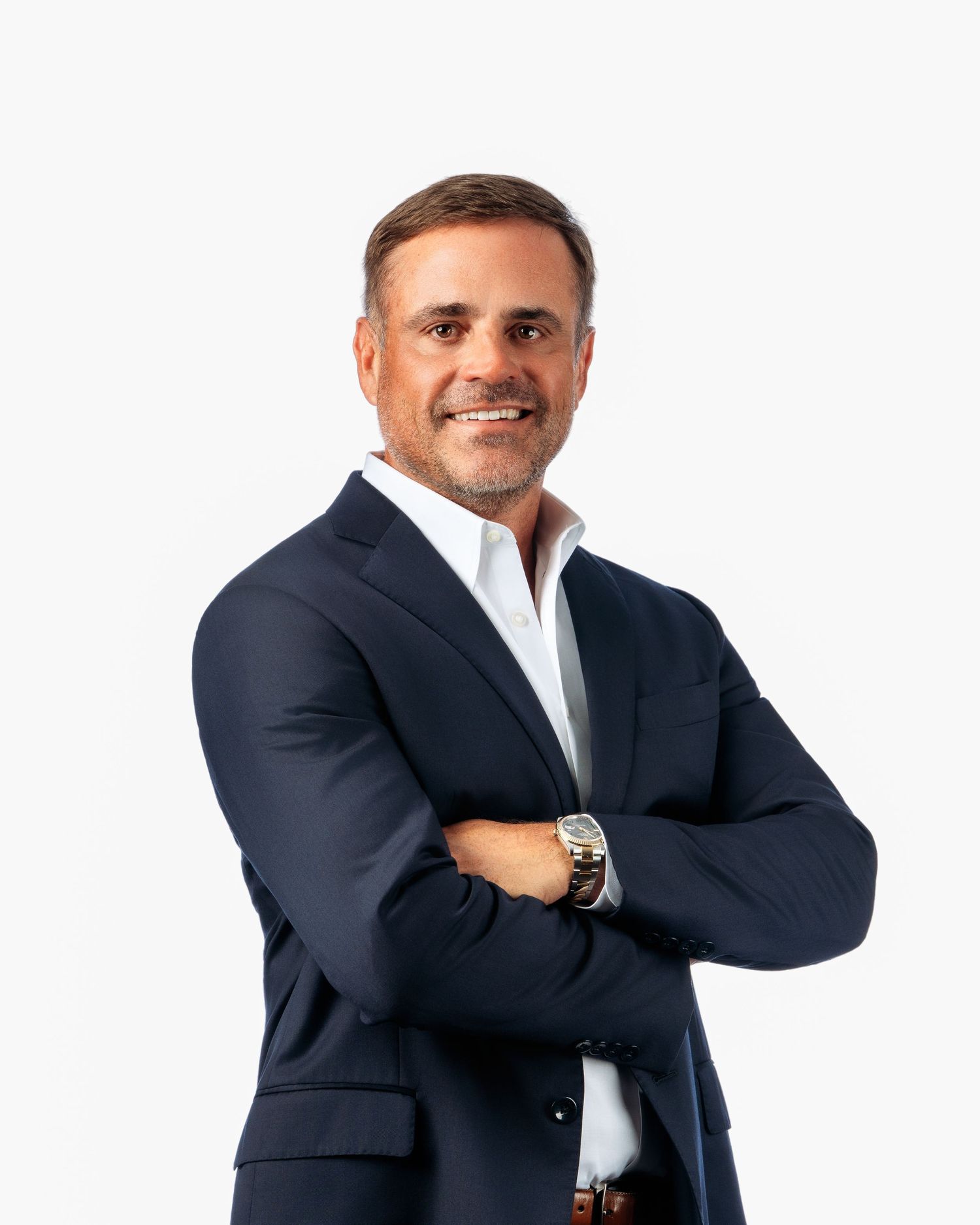 Professional businessman in navy suit with arms crossed, smiling confidently against white background.