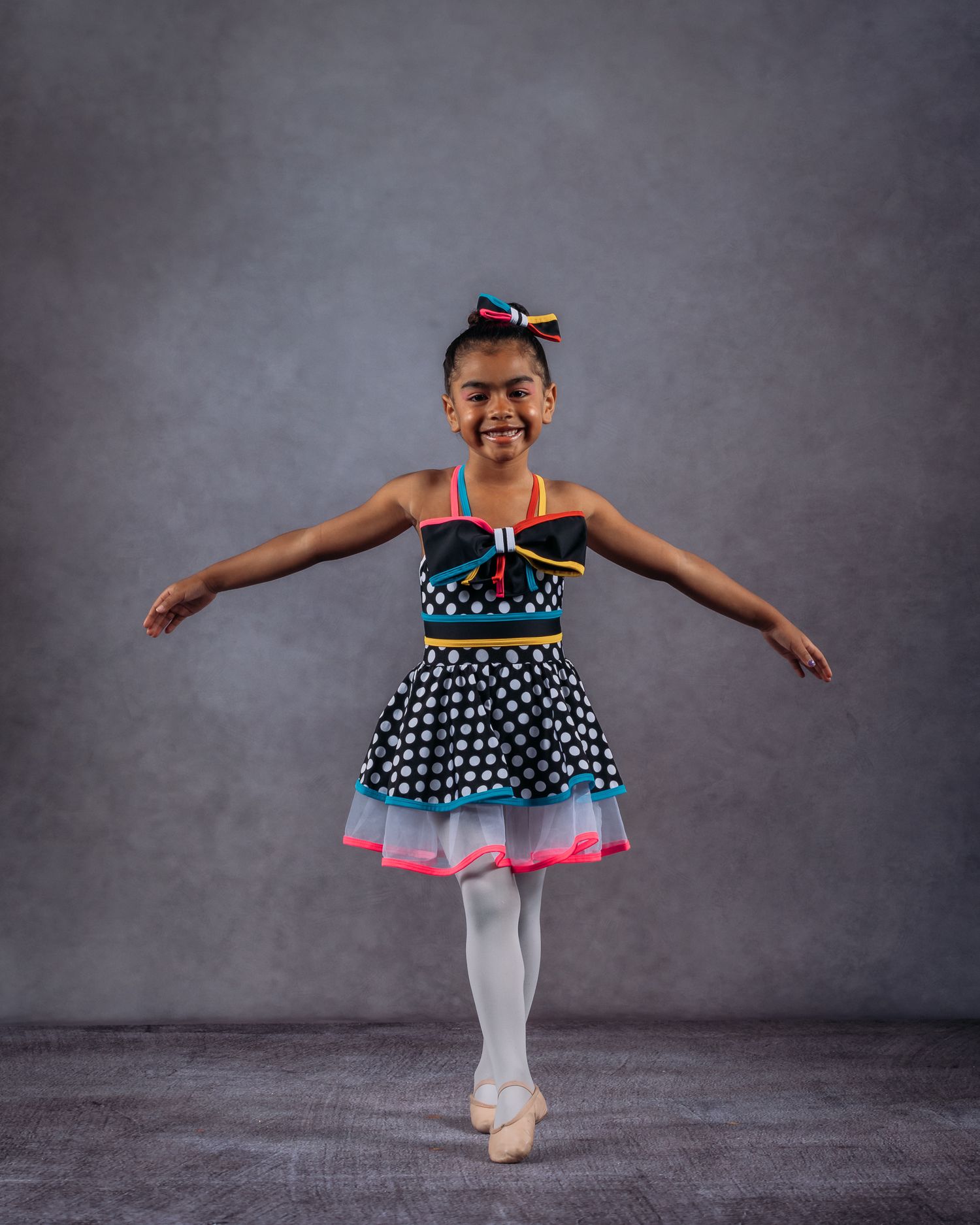 Smiling young ballerina in colorful polka dot tutu dress posing on pointe in studio.