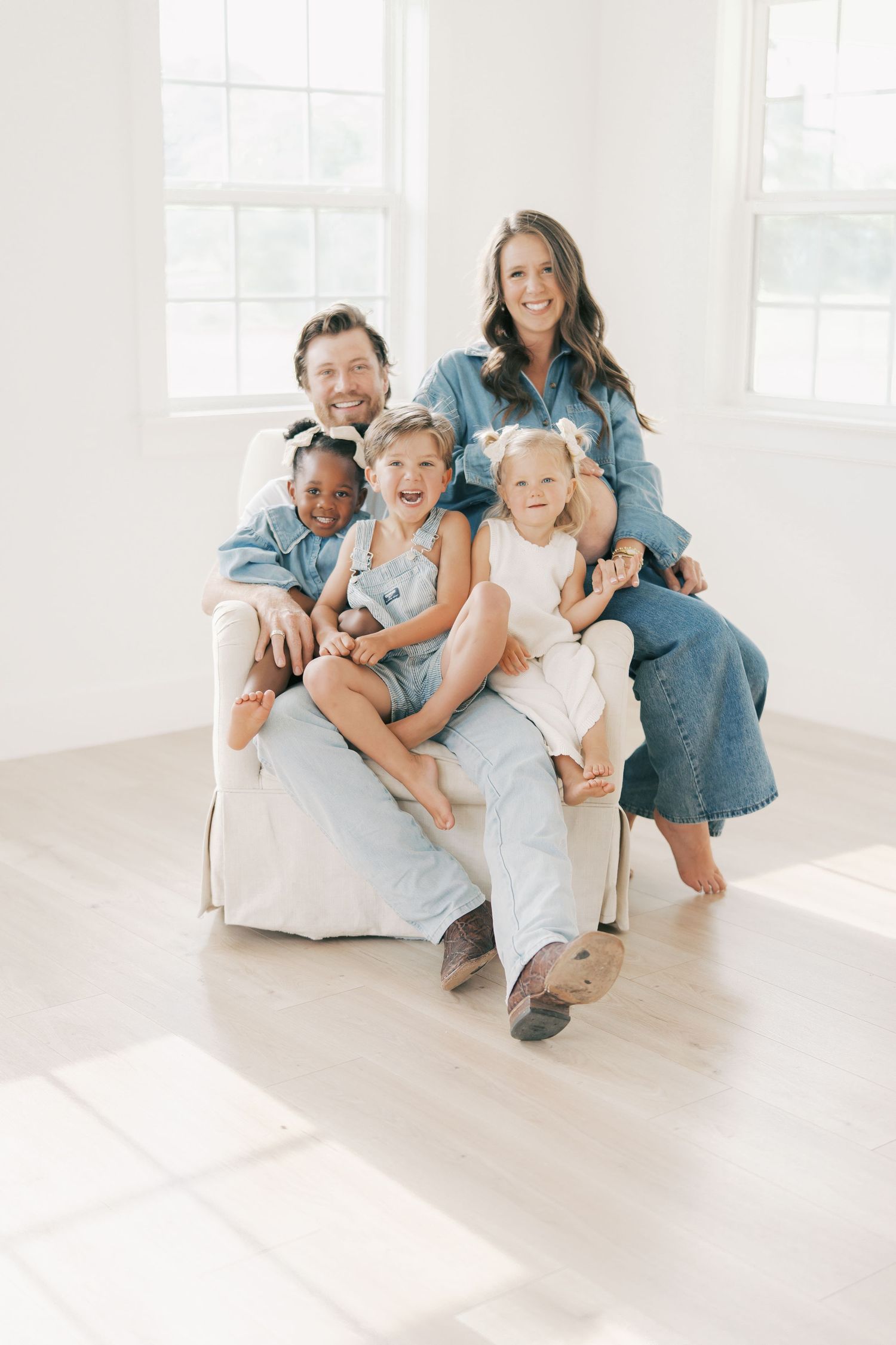 Family of five in denim outfits posing together on a chair indoors by Alahir Villasenor Photographer