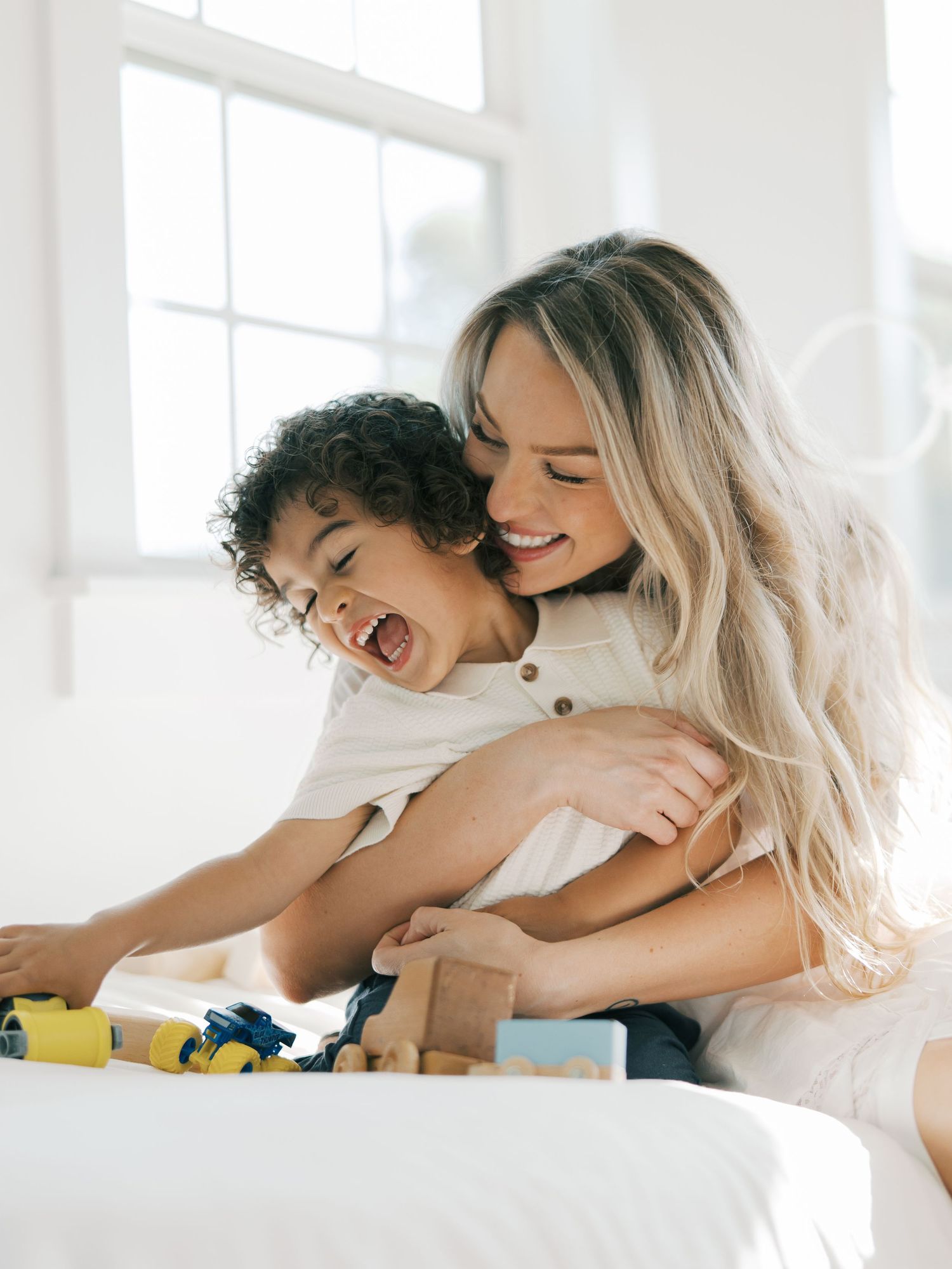 A mother hugs her laughing toddler while playing with wooden toys indoors by Alahir Villasenor Photographer