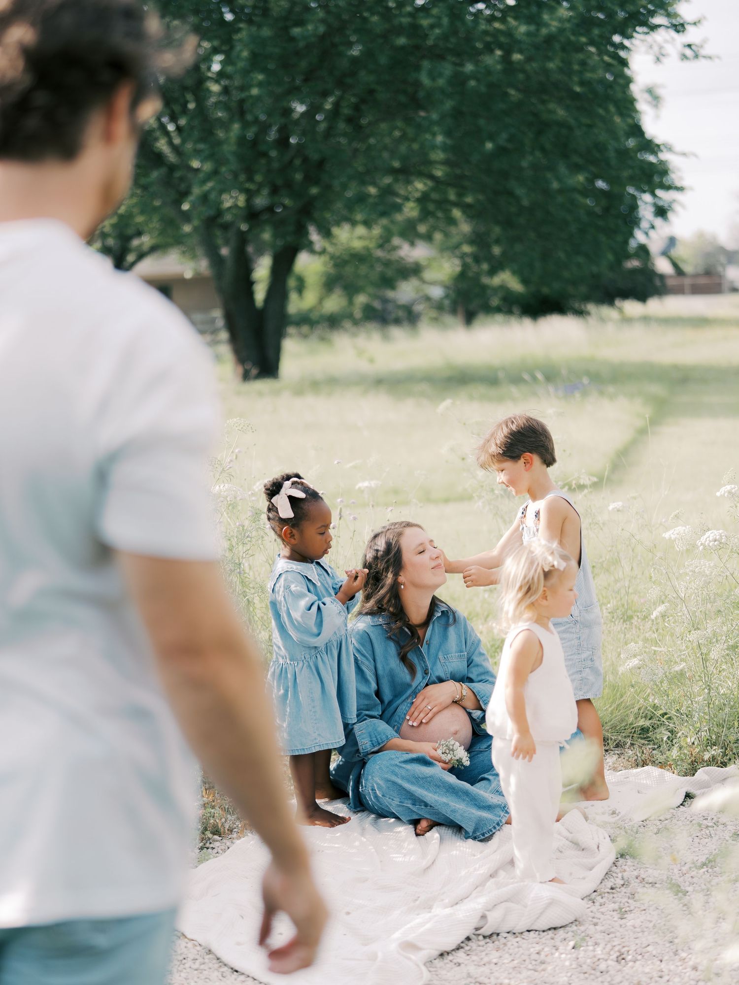 A pregnant mother sits on a blanket in a green field surrounded by her three children in Dallas by Alahir Villasenor Photography.