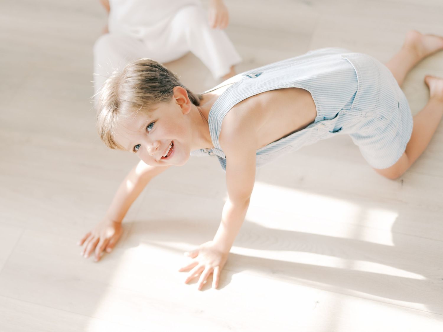 A smiling young child in a gray romper plays on a sunlit hardwood floor in Dallas by Alahir Villasenor Photography.