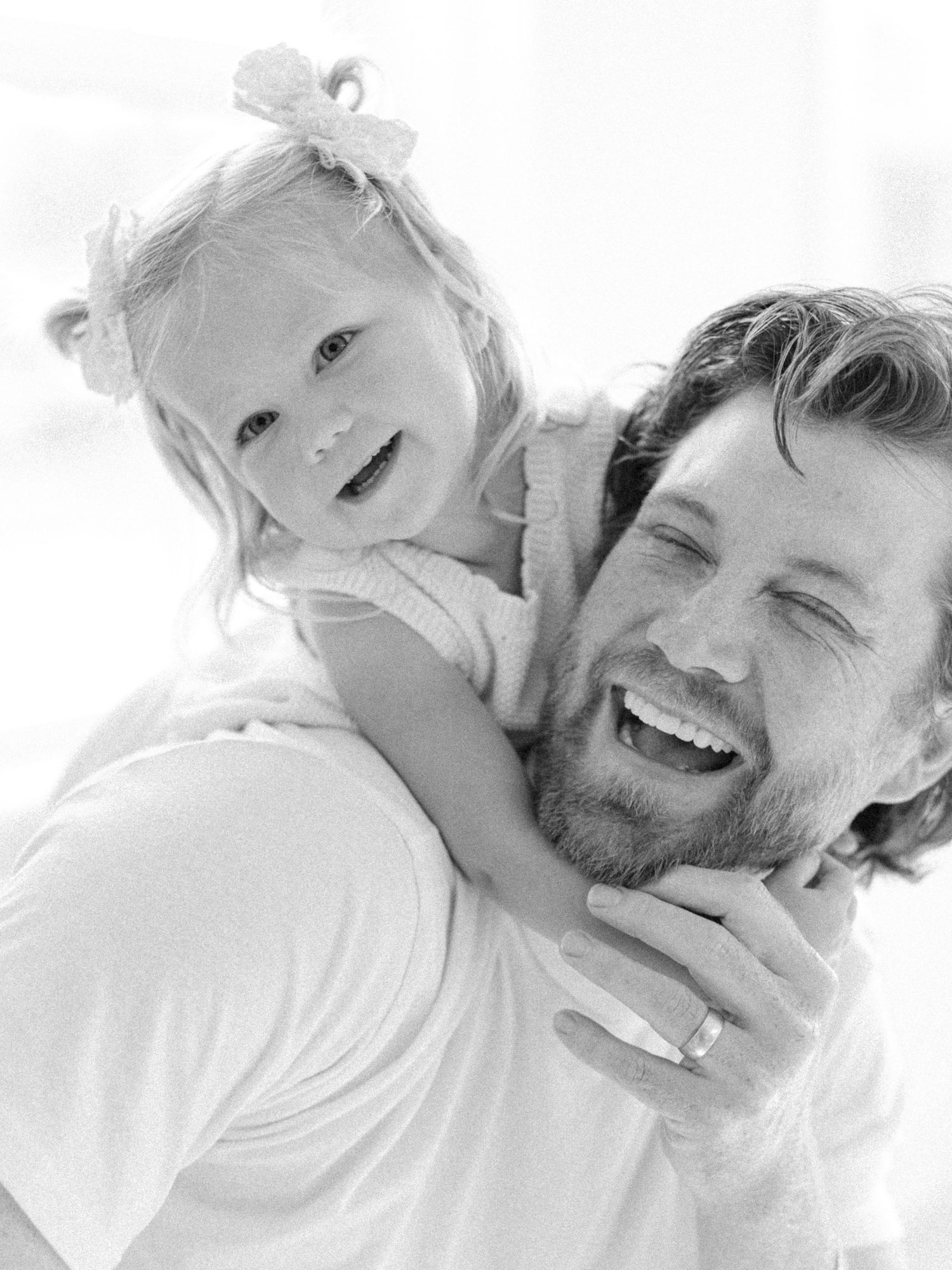 Black and white photo of a bearded father laughing with his little girl on his back by Alahir Villasenor Photographer