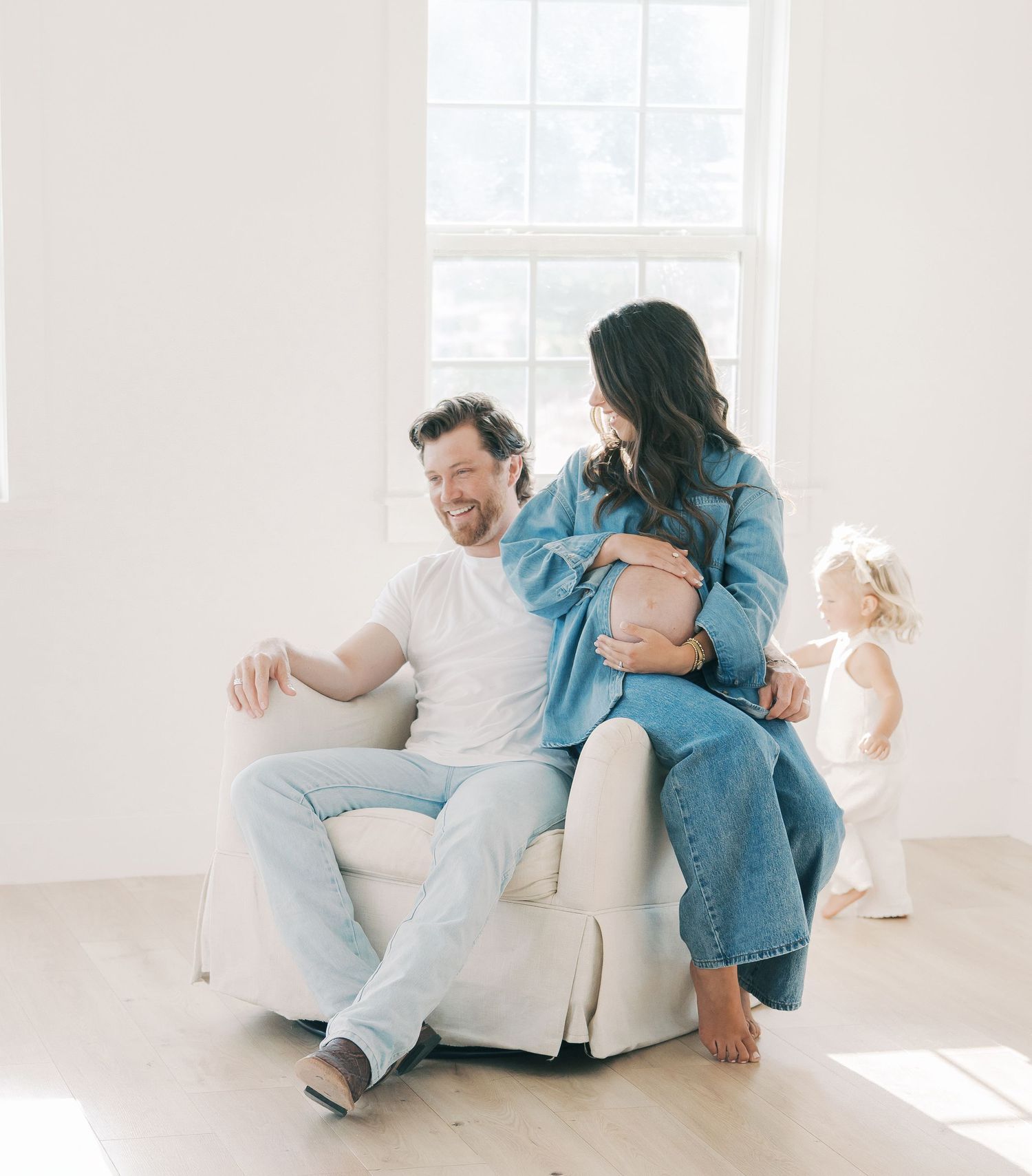 Couple shares a tender moment with pregnant belly as toddler plays nearby in studio in Dallas by Alahir Villasenor Photography-Family Sessio