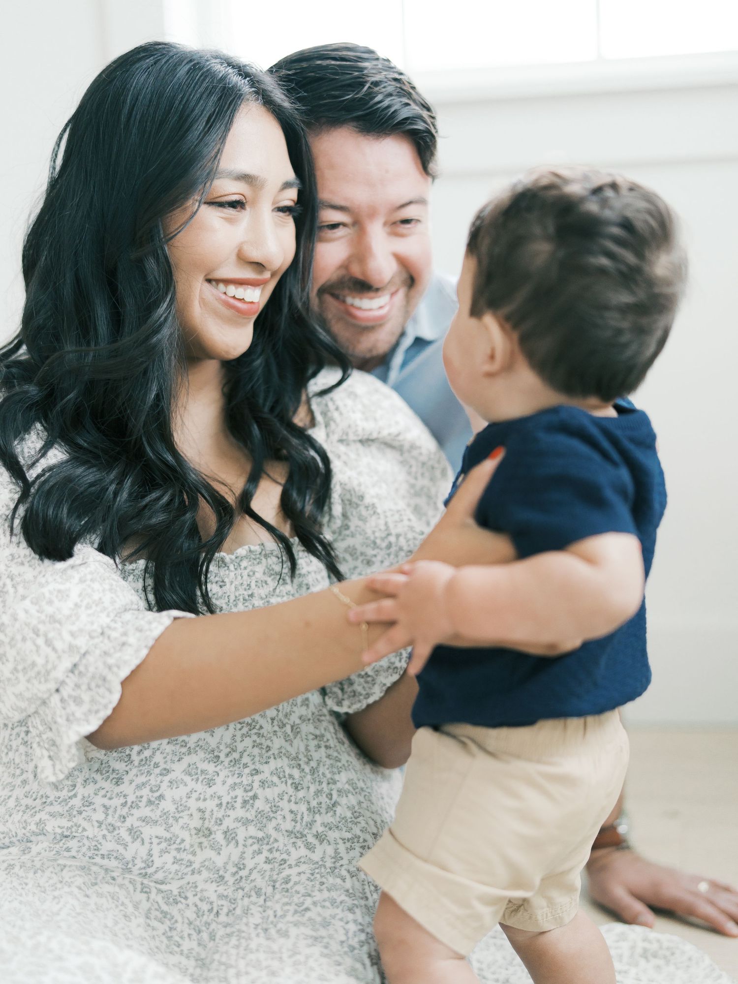 Smiling parents holding their baby boy during a bright and airy family photo session.