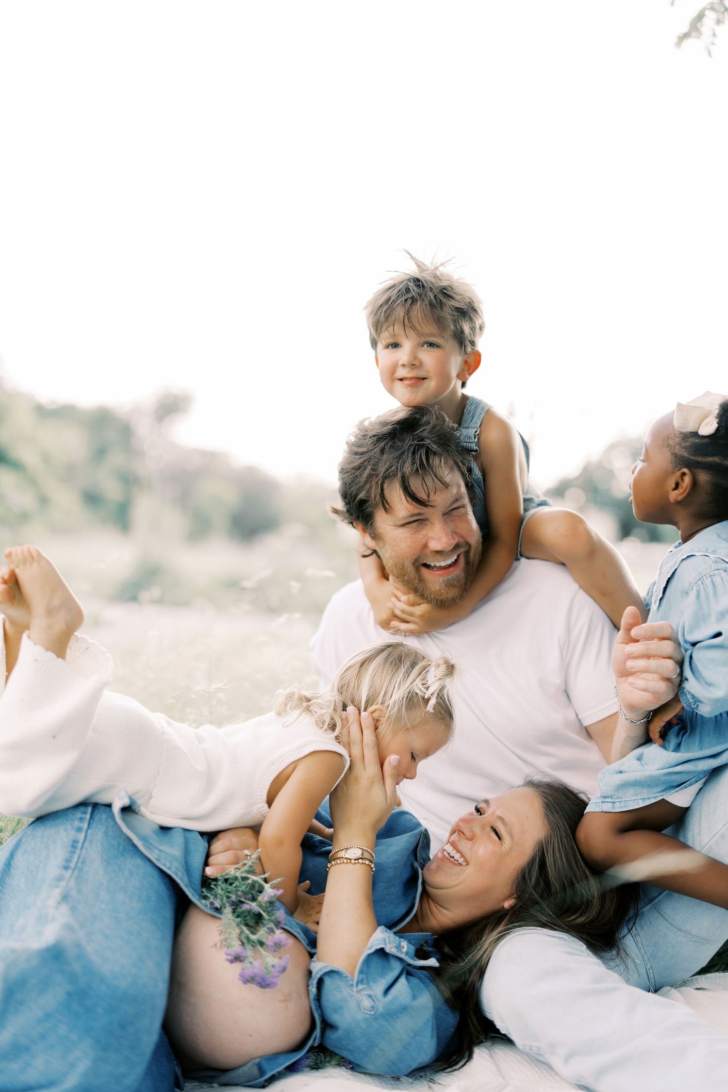A joyful family of five laughs and cuddles together on a sunny outdoor blanket in Dallas by Alahir Villasenor Photography.