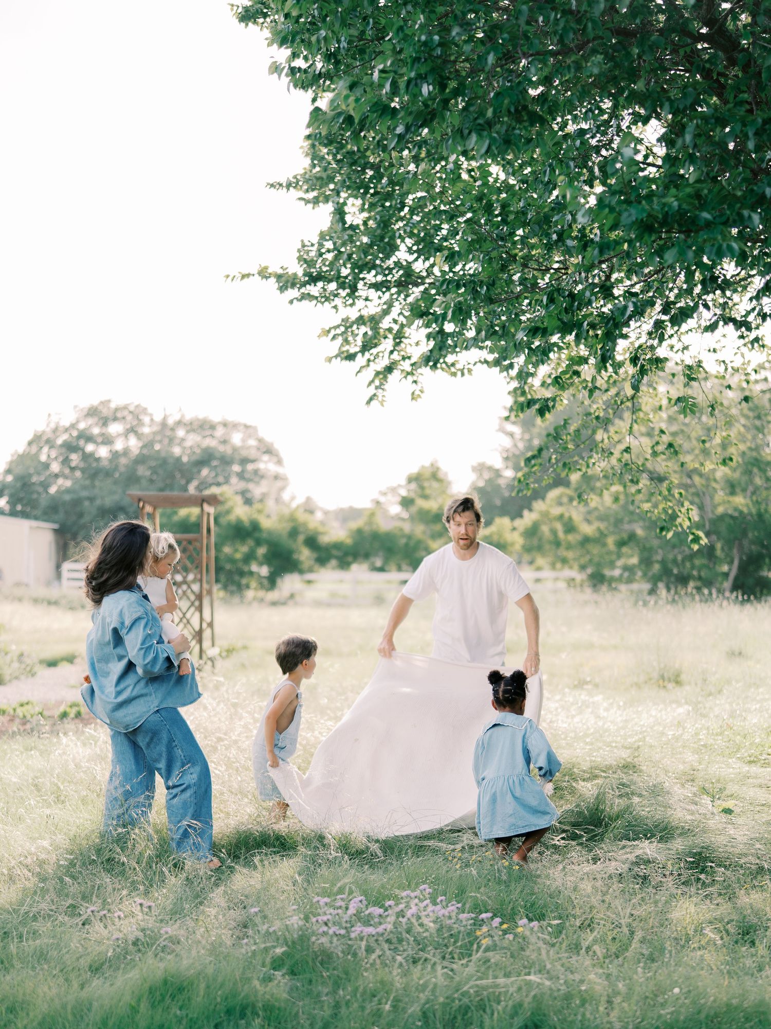 A family of five gathers around a white blanket in a lush green meadow in Dallas by Alahir Villasenor Photography.