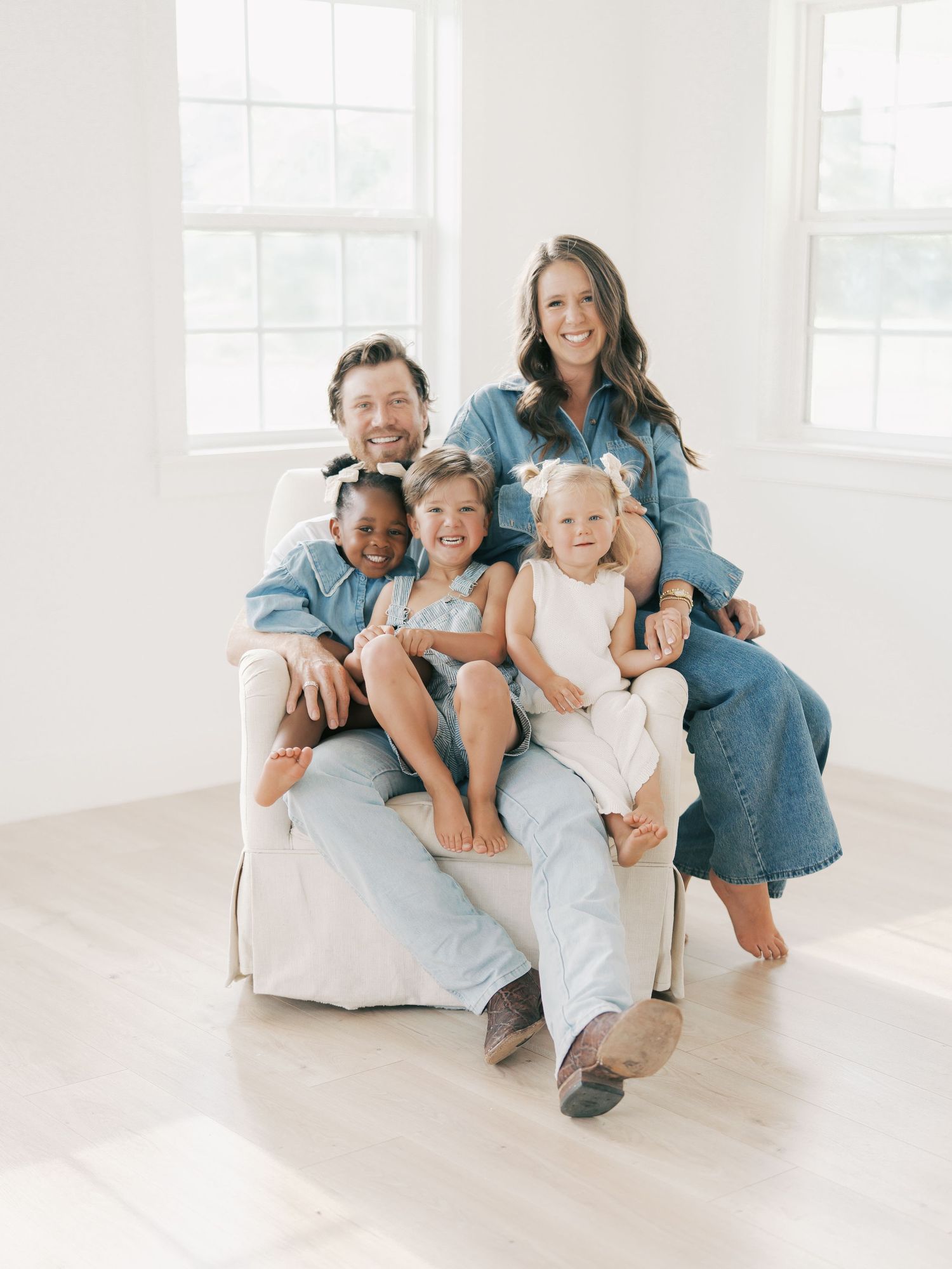 Smiling family of five in coordinated denim outfits poses in a bright white studio in Dallas by Alahir Villasenor Photography-Family Session