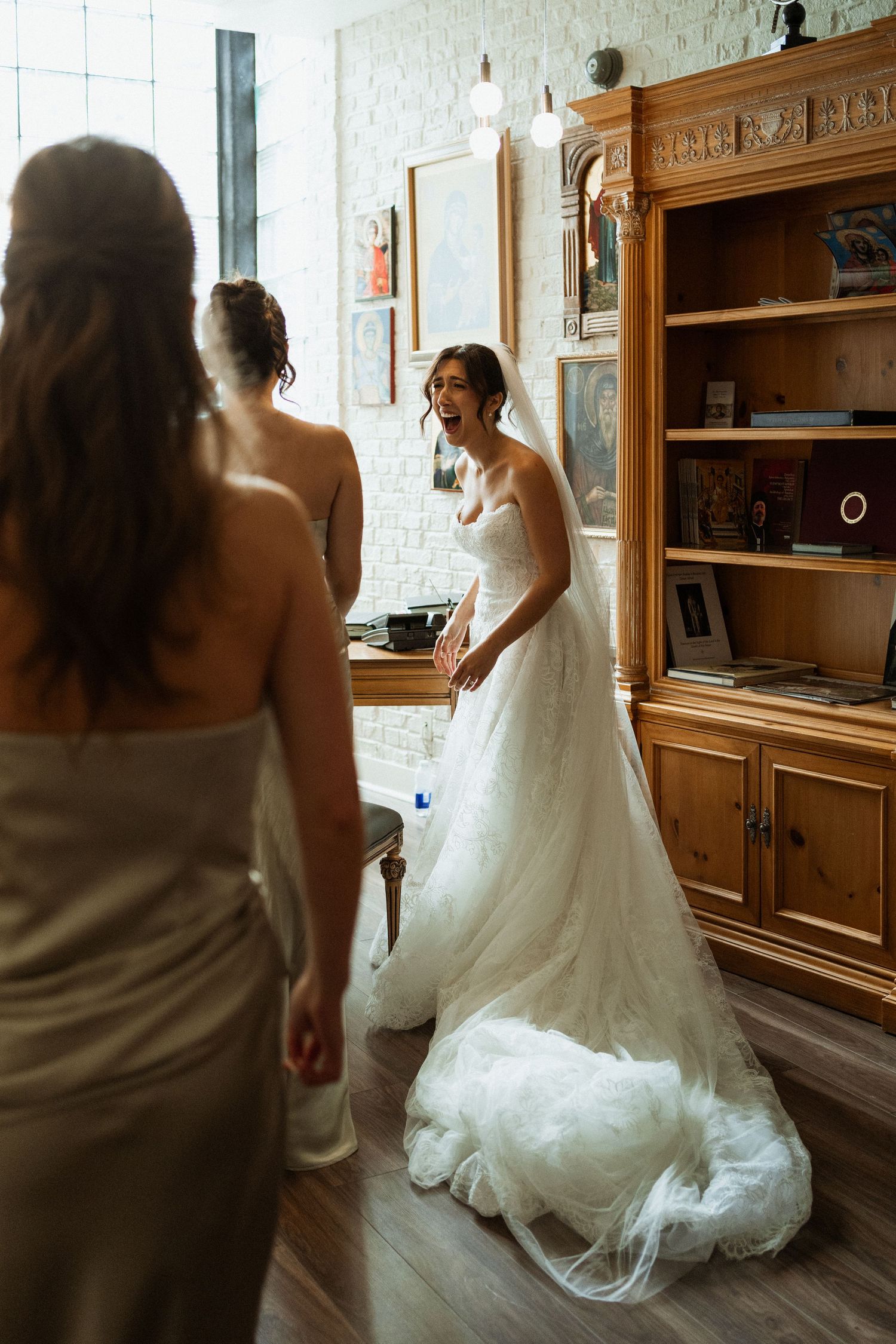 Bride in lace ball gown smiling at bridesmaid during wedding morning preparations.