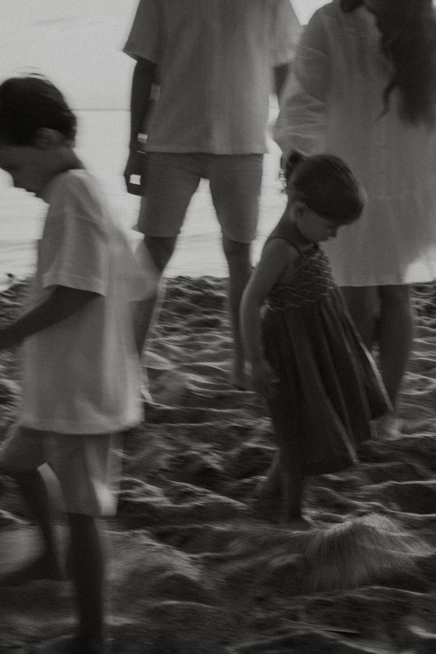 Black and white photo of children and adults walking on a rocky beach together.