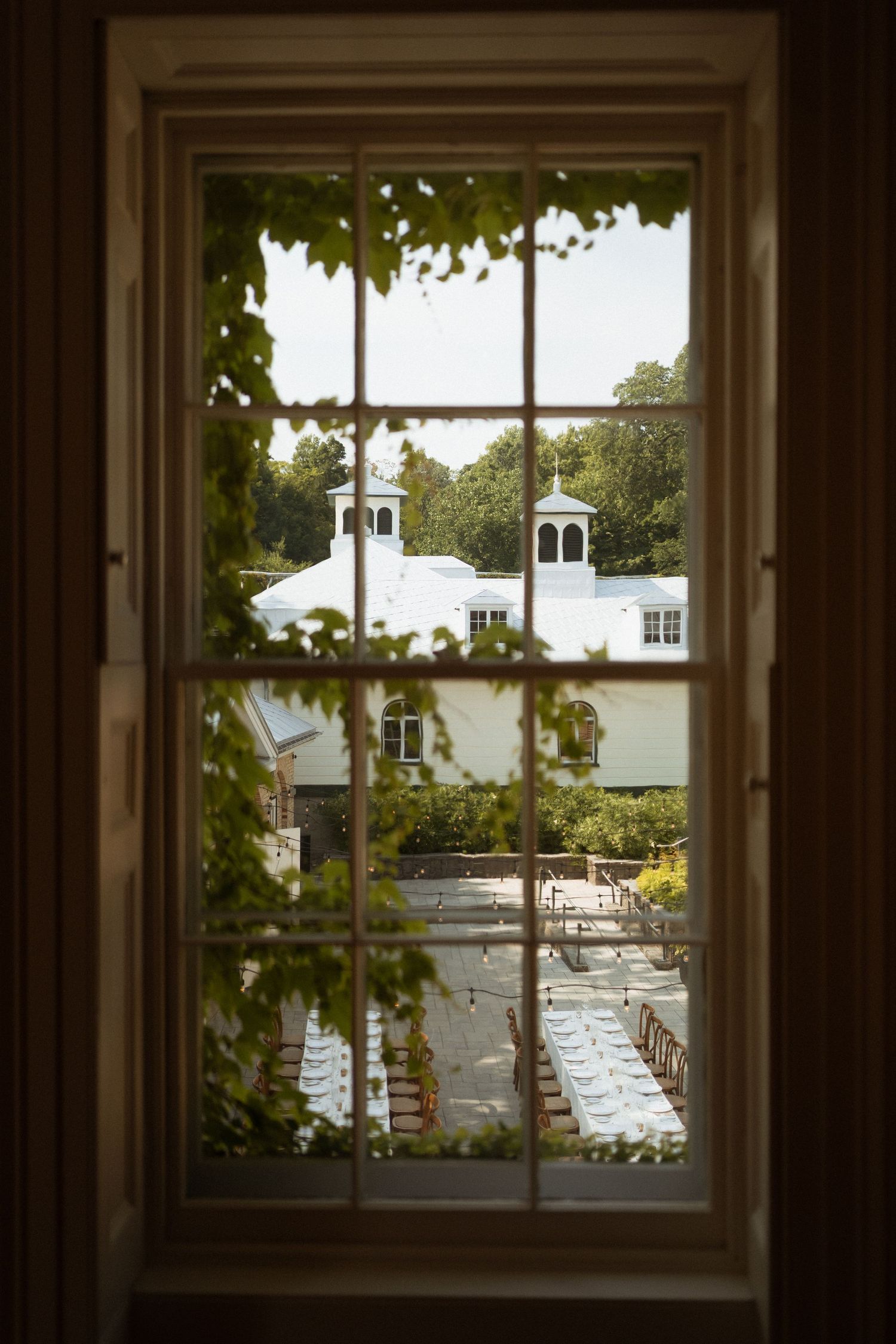 View through a multi-pane window of an outdoor wedding ceremony setup with white chairs and a cupola building.