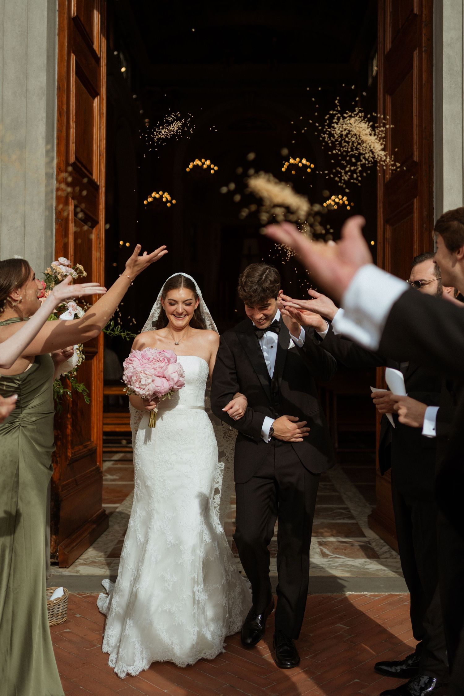 Newlyweds exit church doors as guests toss rice in joyful wedding send-off celebration.