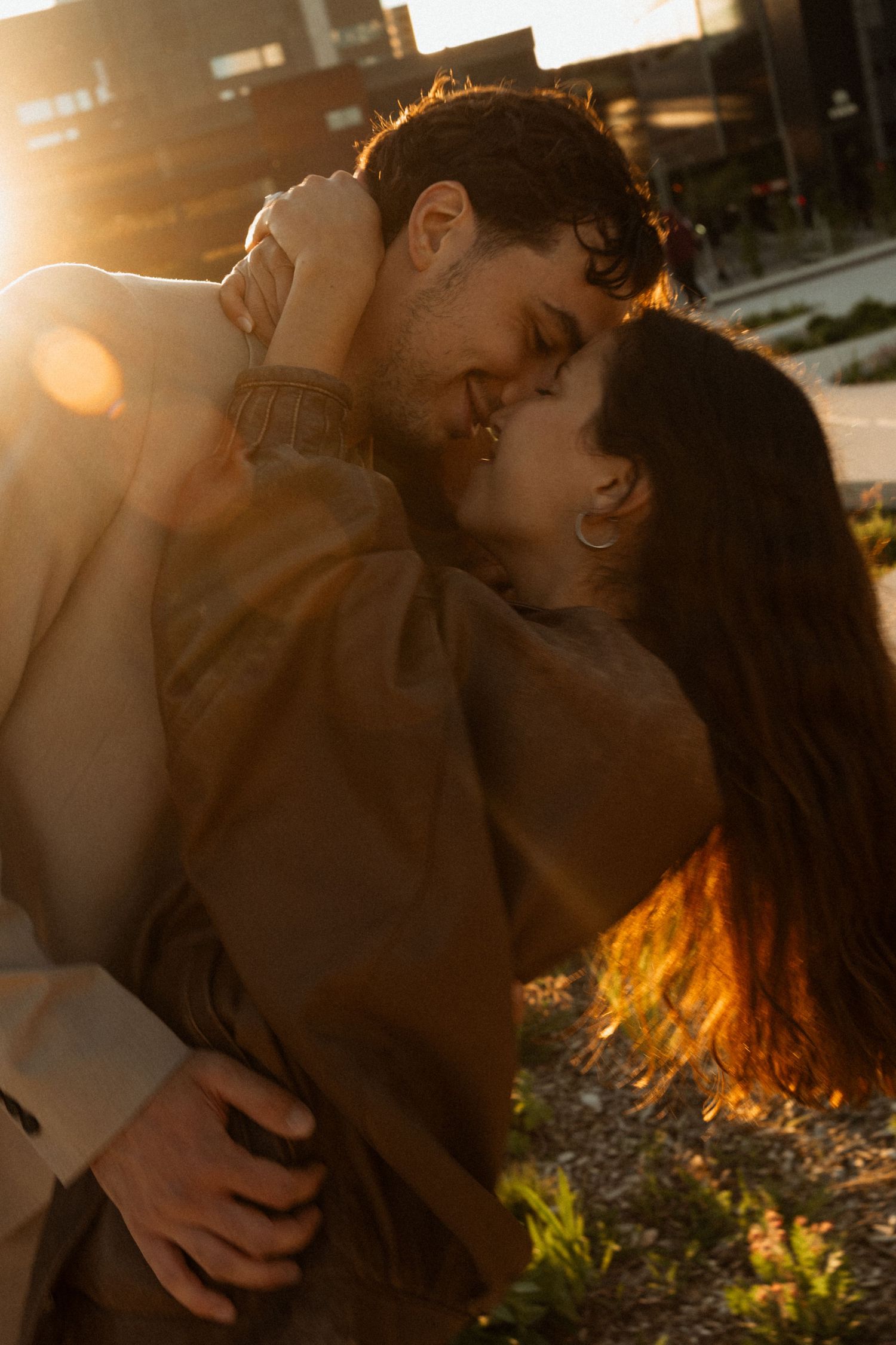 A couple shares a romantic almost-kiss embrace outdoors bathed in warm golden sunset light.