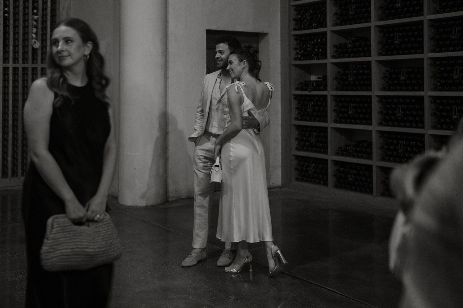 Couple embracing and smiling at a wedding reception in a wine cellar, captured in black and white.