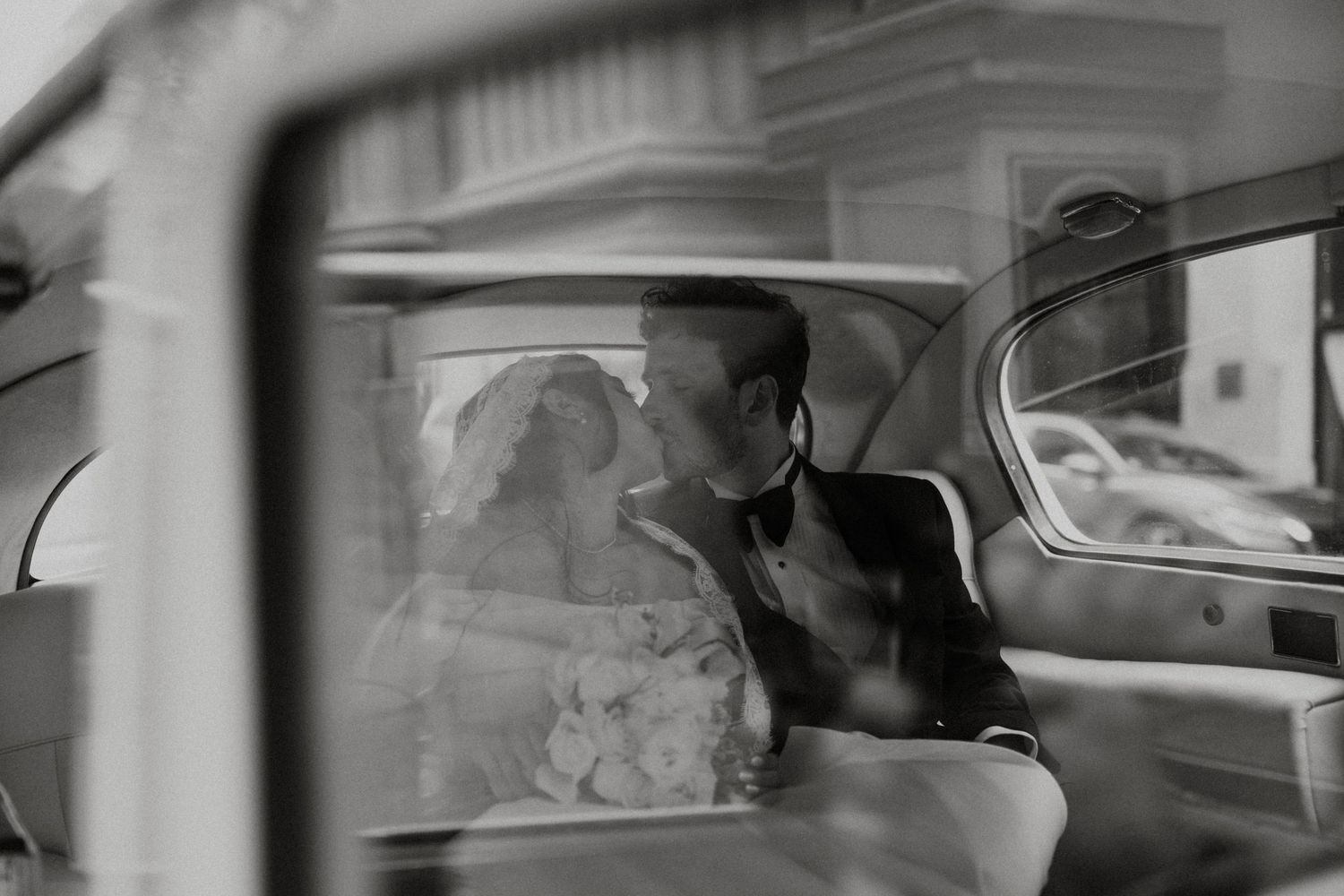 Black and white artistic photo of bride and groom sharing intimate moment inside vintage wedding car.