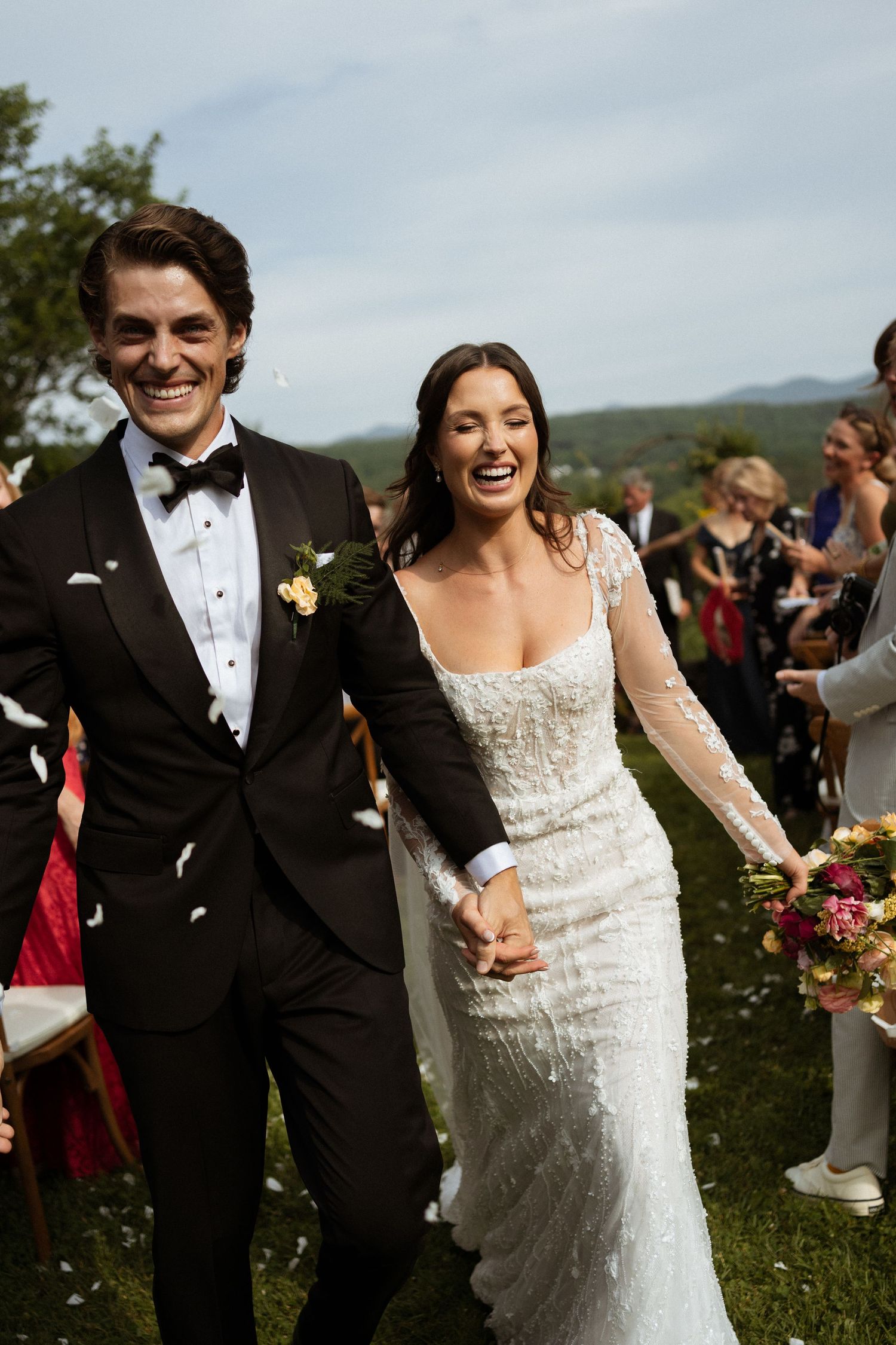 Happy bride and groom walking down outdoor aisle with guests throwing confetti.