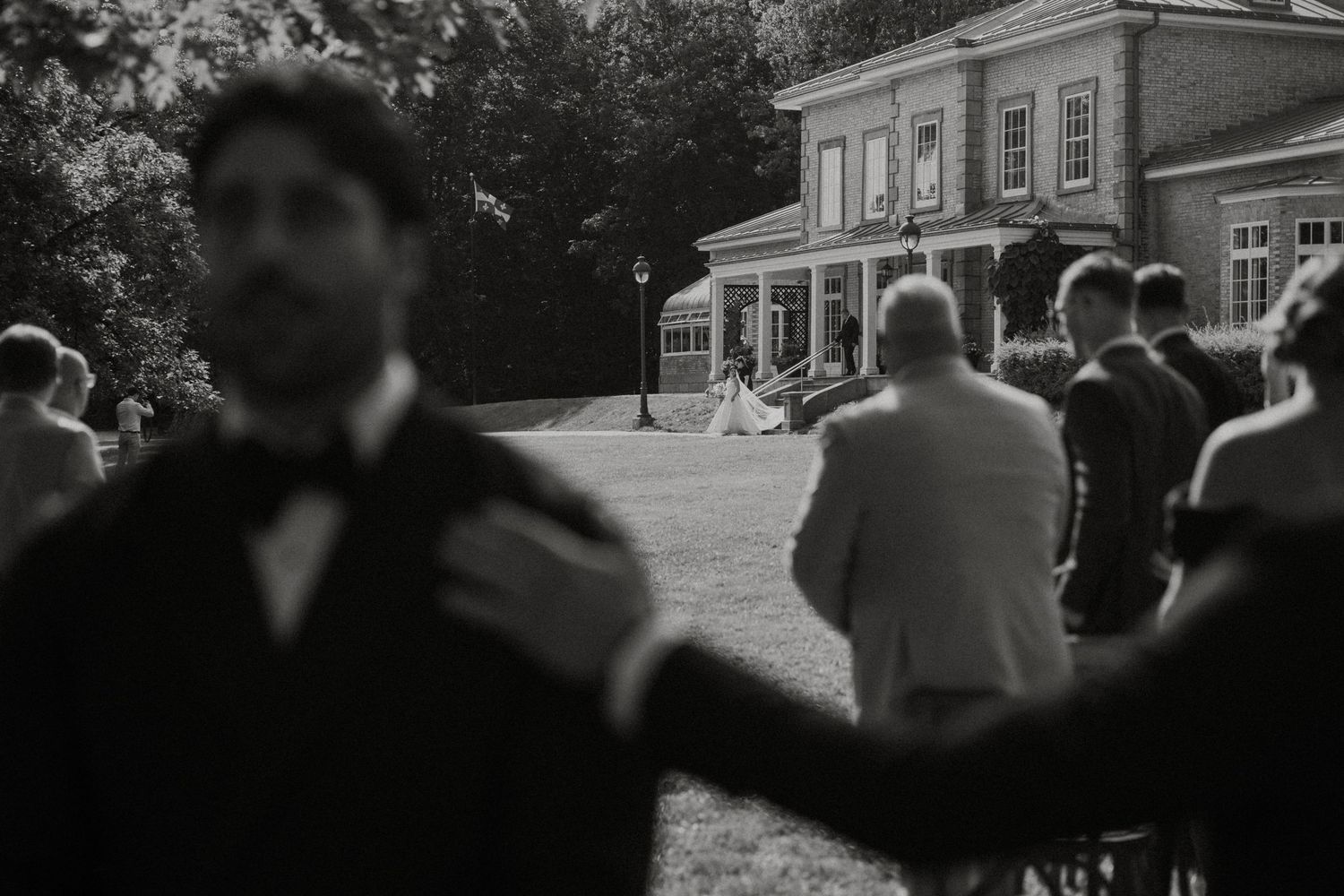 Black and white wedding photo of guests gathered on a lawn outside an elegant venue building.