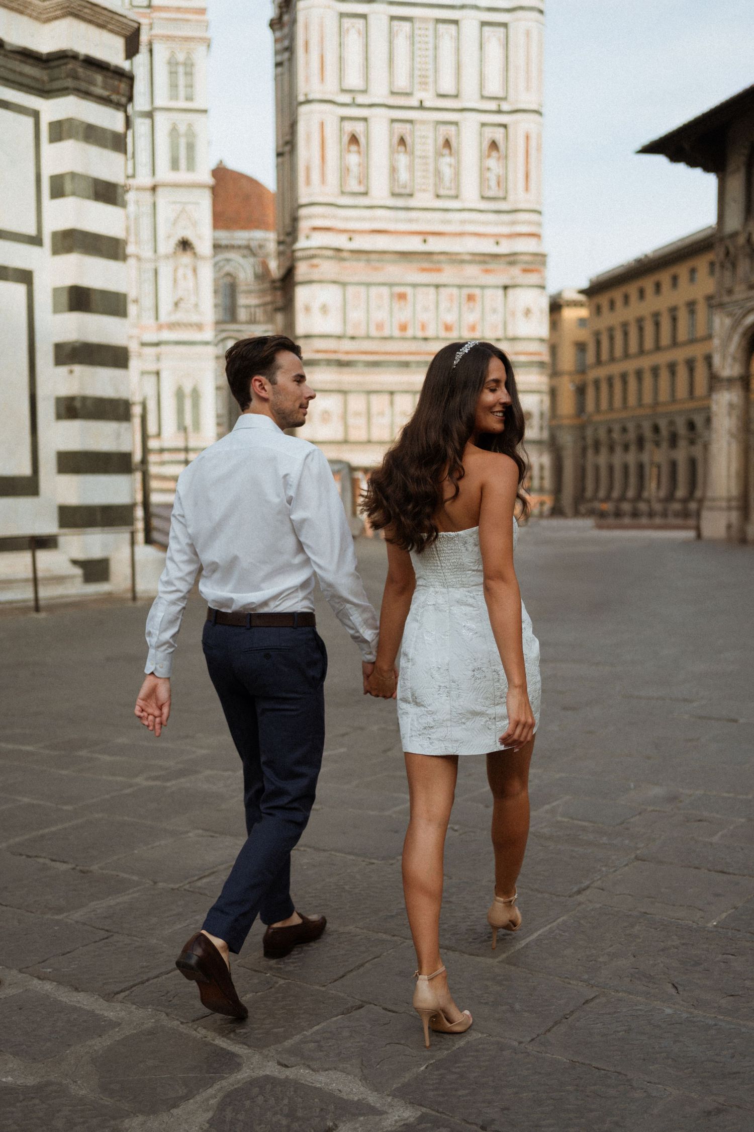 Couple walking hand in hand near Florence Cathedral Duomo on cobblestone piazza.