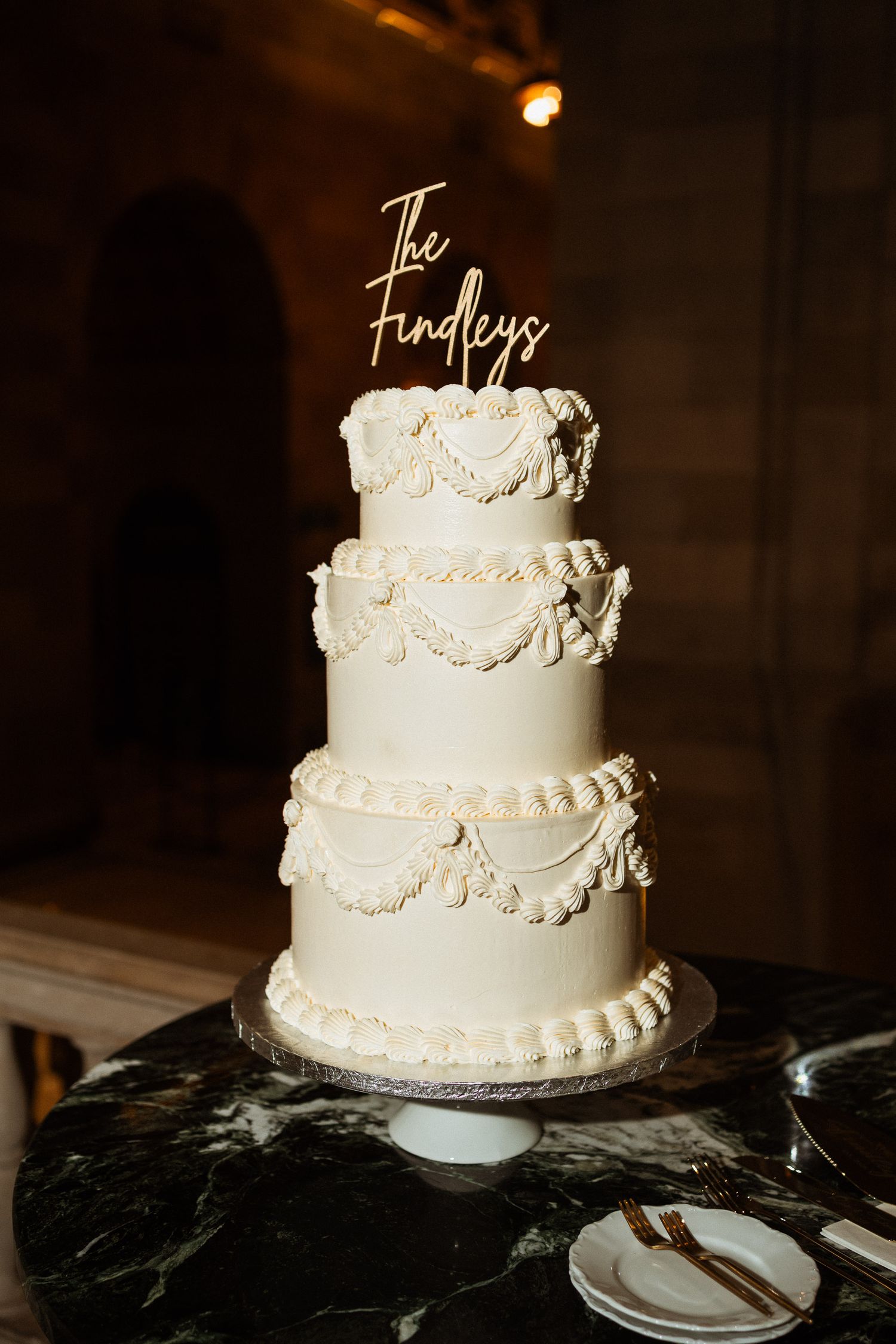 Three-tier white wedding cake with lambeth piping and gold custom topper reading The Findleys.