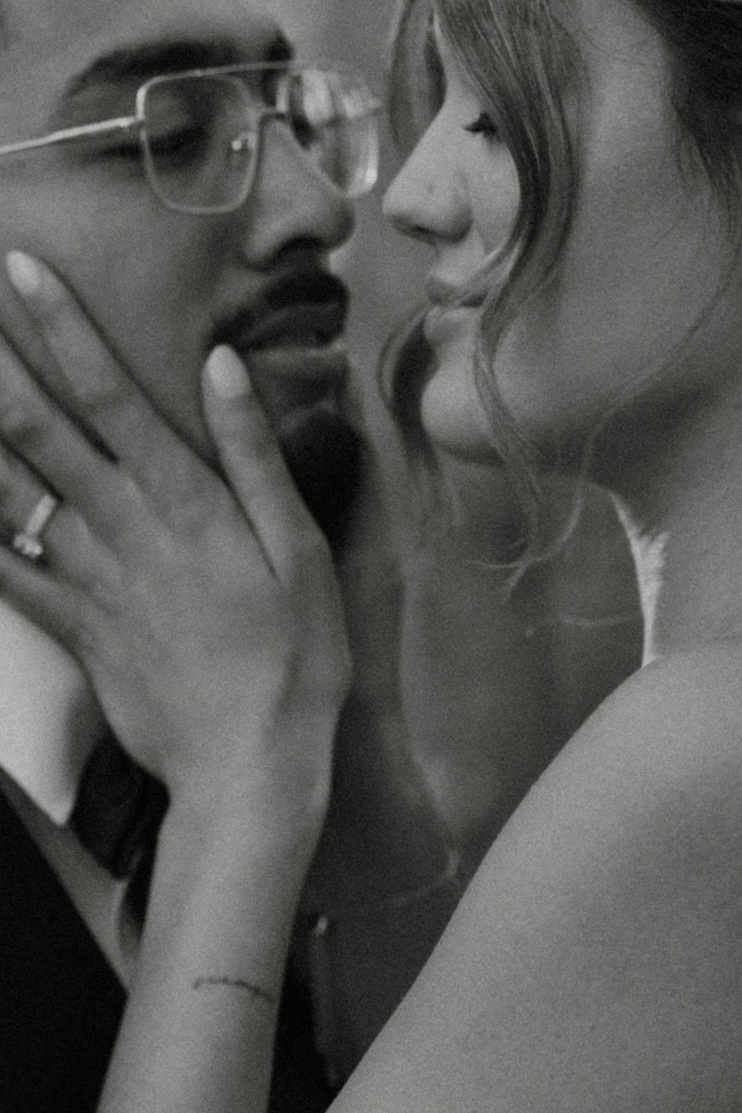 Black and white photo of a couple in an intimate moment, woman with ring and wrist tattoo touching mans face.