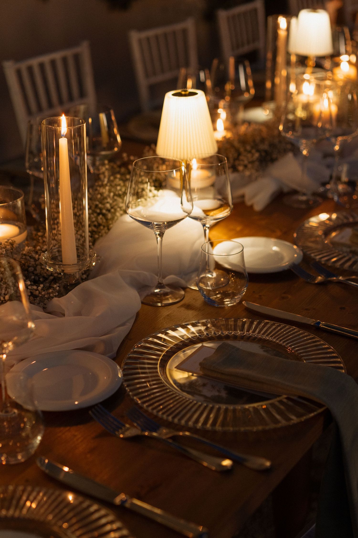 Elegant candlelit dinner table set with gold charger plates, crystal glasses, white napkins, and glowing candles for a formal event.