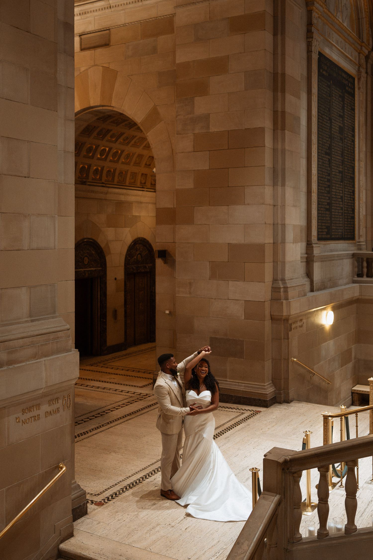 Bride and groom dancing in an elegant grand hall with ornate stone arches and marble floors.