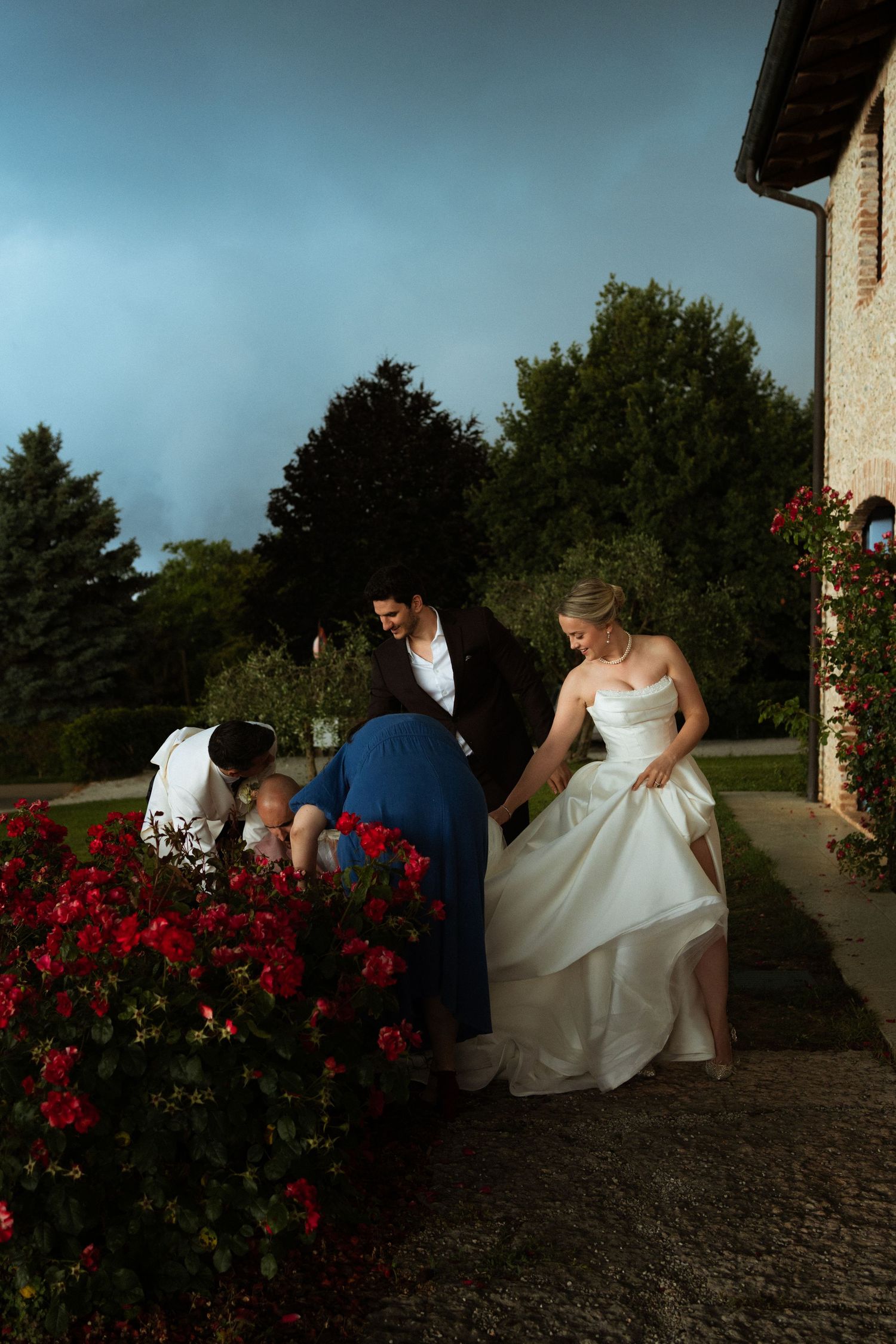 Bride and wedding guests rushing indoors past red roses under a dramatic stormy sky.