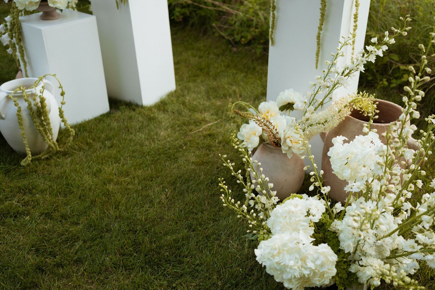Elegant outdoor wedding ceremony decor with white floral arrangements in terracotta pots on lush green grass.