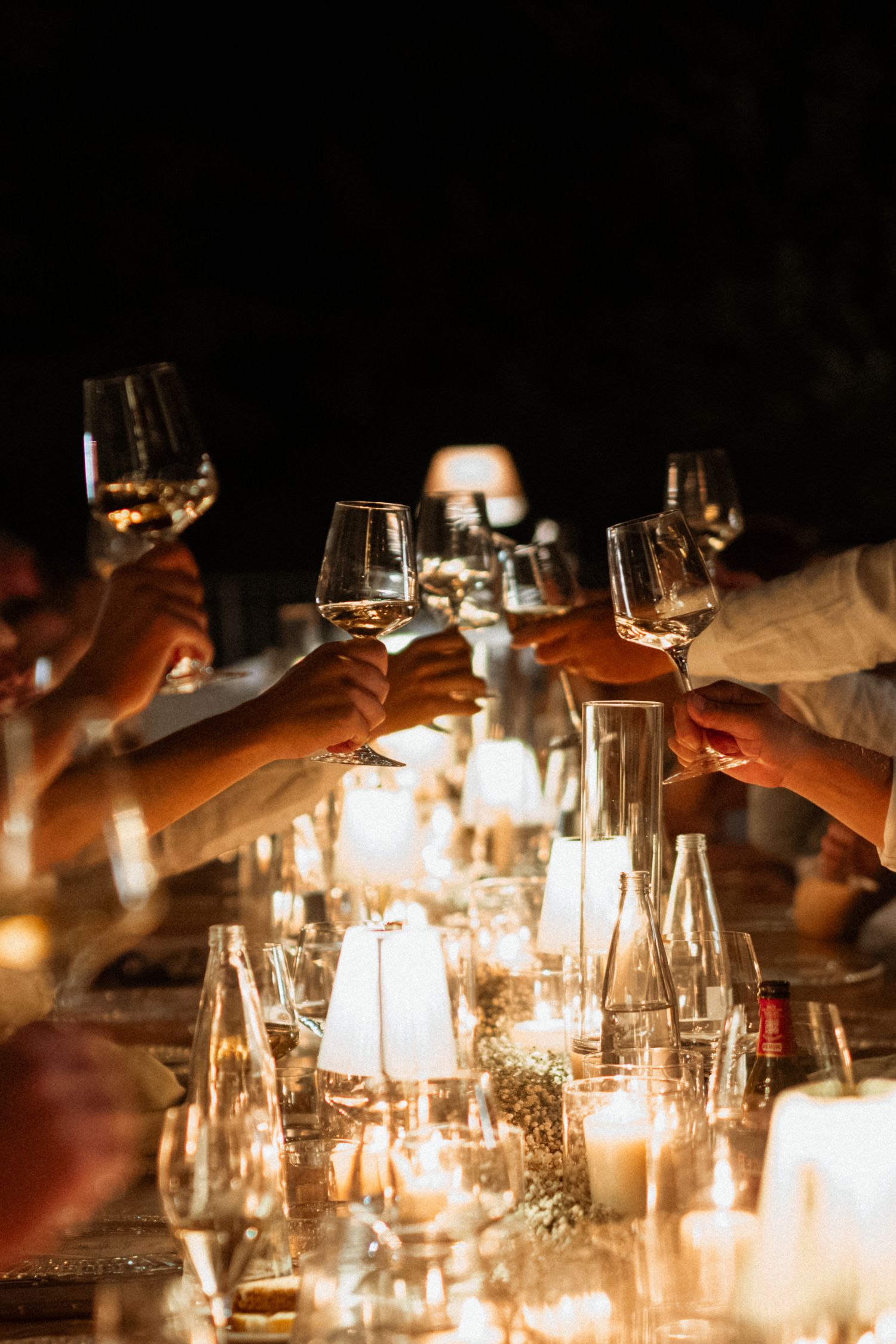 Guests raising wine glasses in a candlelit toast at an elegant dinner party with glowing candles on the table.
