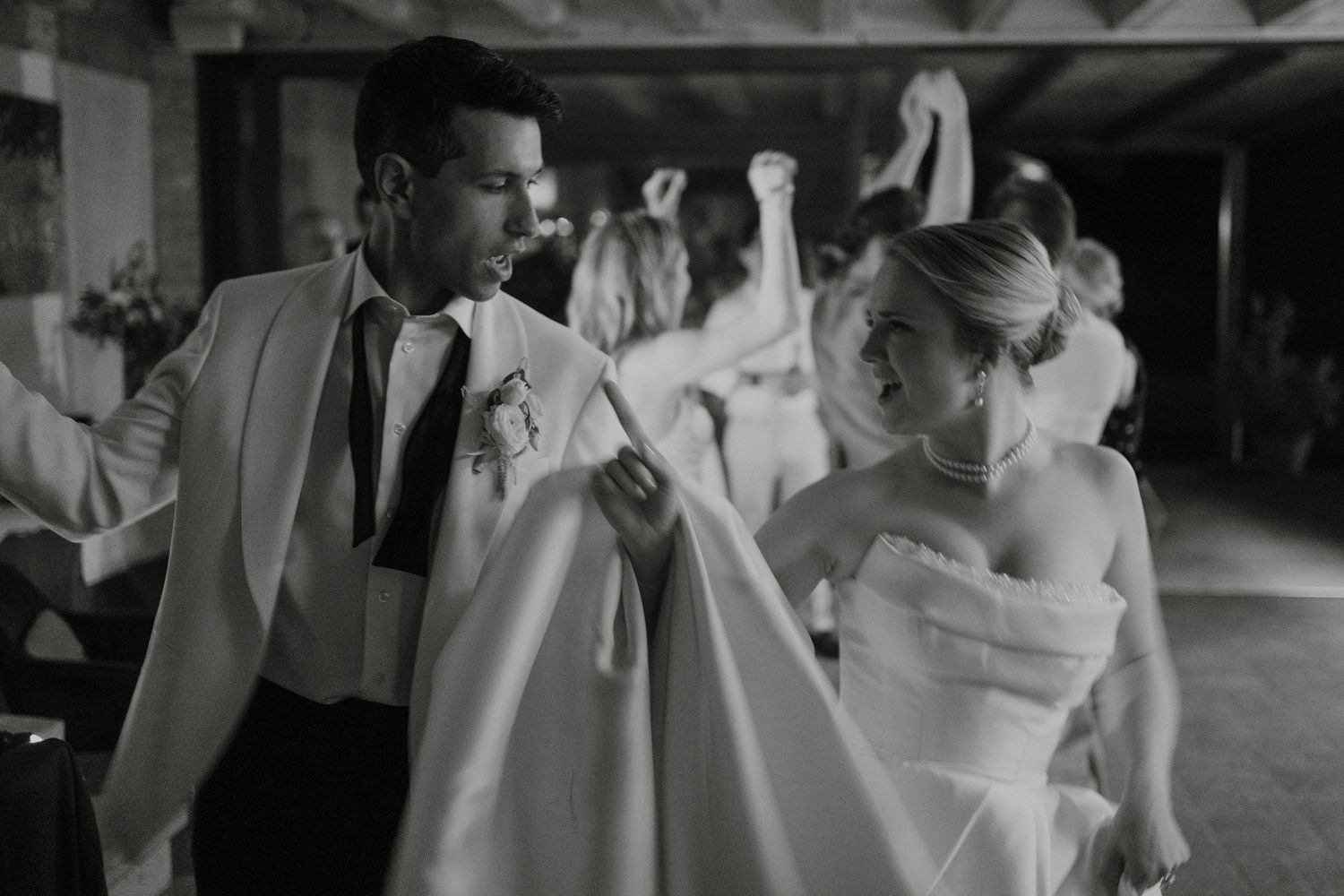 Black and white photo of a bride and groom dancing joyfully at their wedding reception.