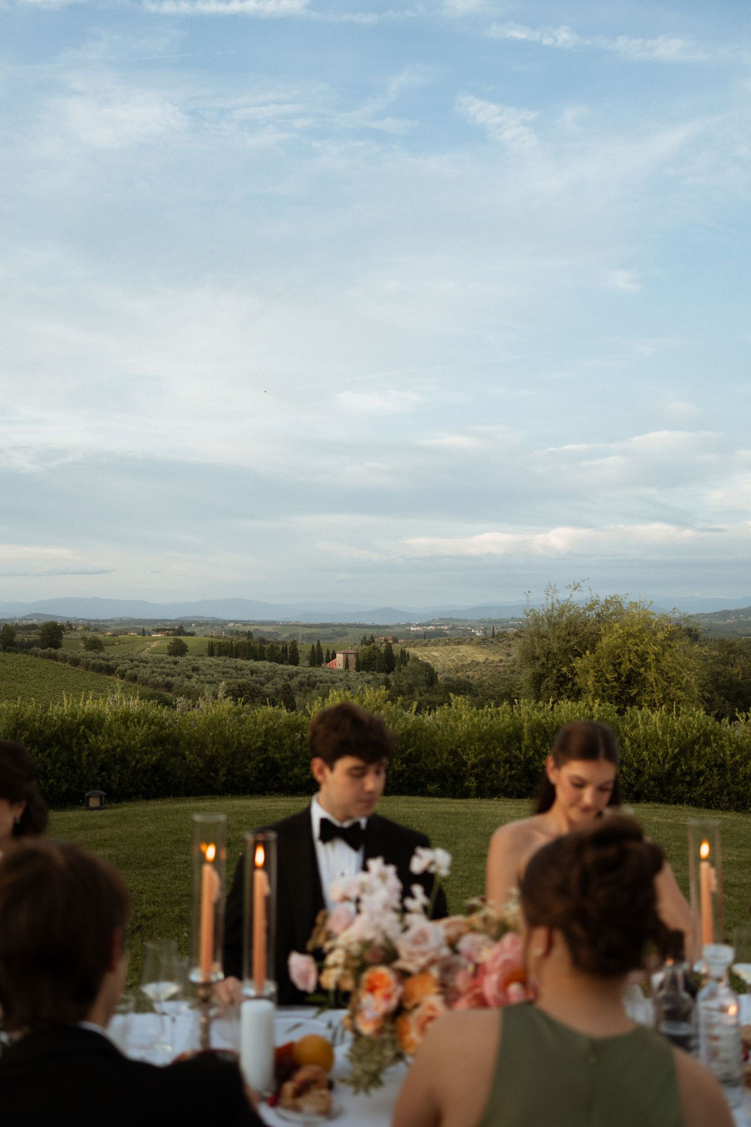 Elegant outdoor wedding reception in Tuscany with candles, floral centerpieces, and rolling vineyard landscape at dusk.