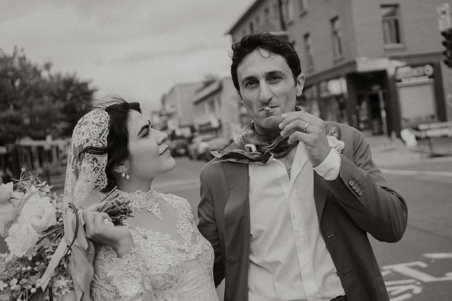 Black and white photo of a bride and groom eating outdoors on their wedding day on a city street.