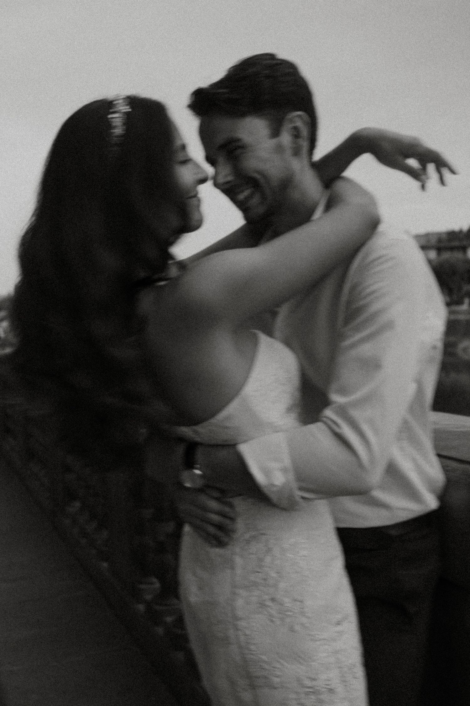 Black and white photo of a laughing couple embracing romantically outdoors.