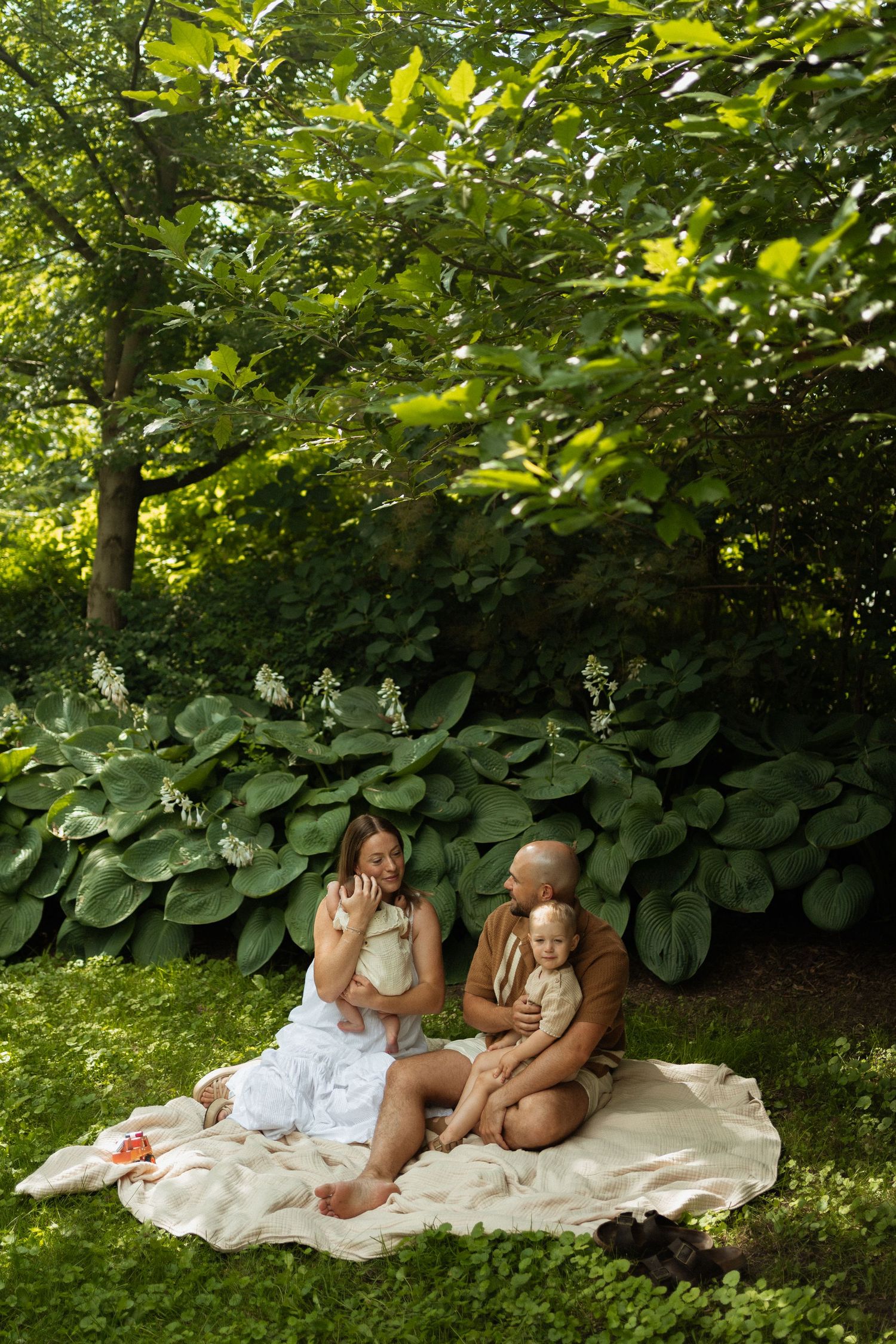A happy family enjoying a picnic on a blanket in a lush green garden with large leafy plants.