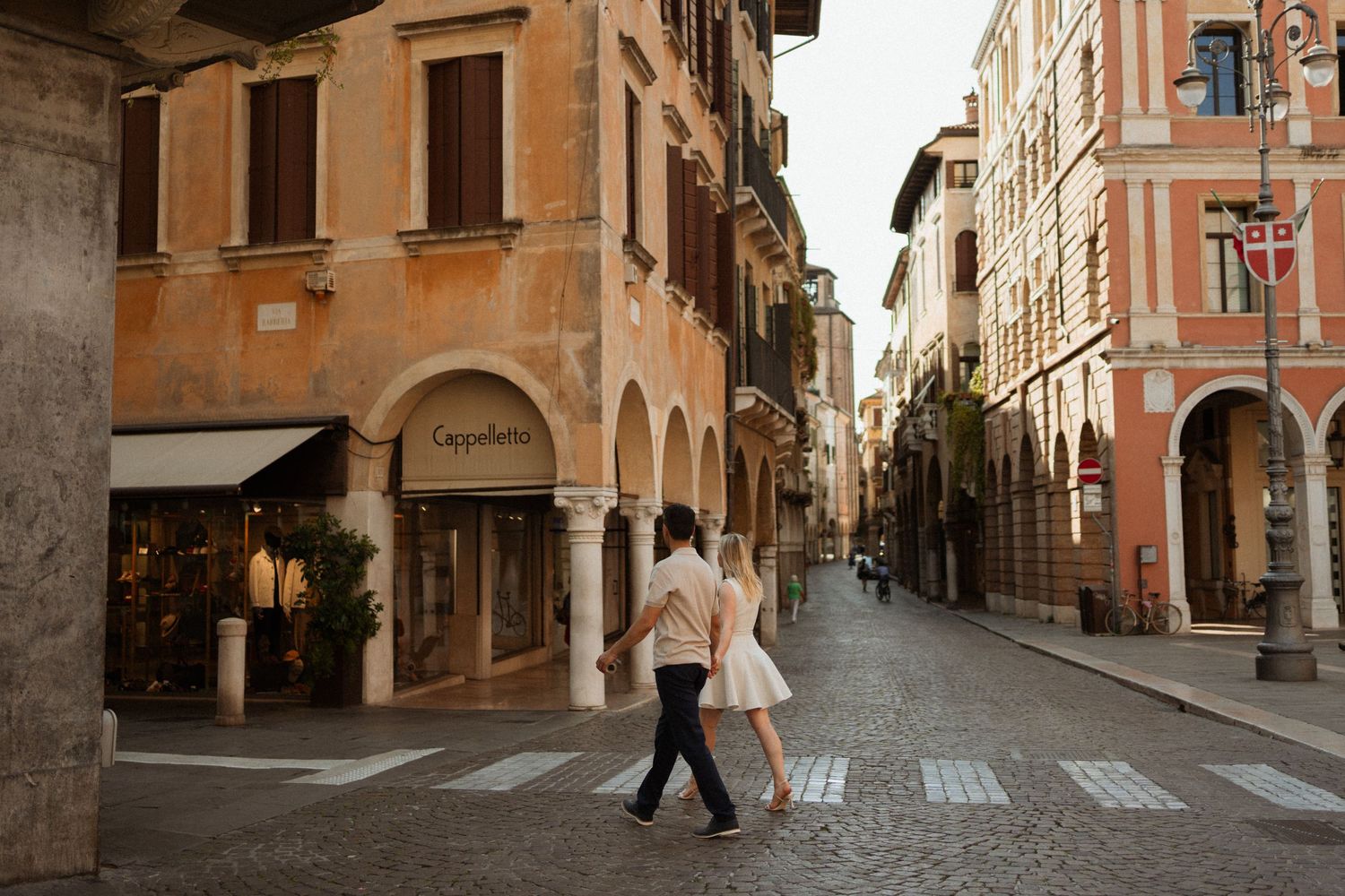 Couple walking hand in hand on a cobblestone street in a charming Italian town with historic buildings.