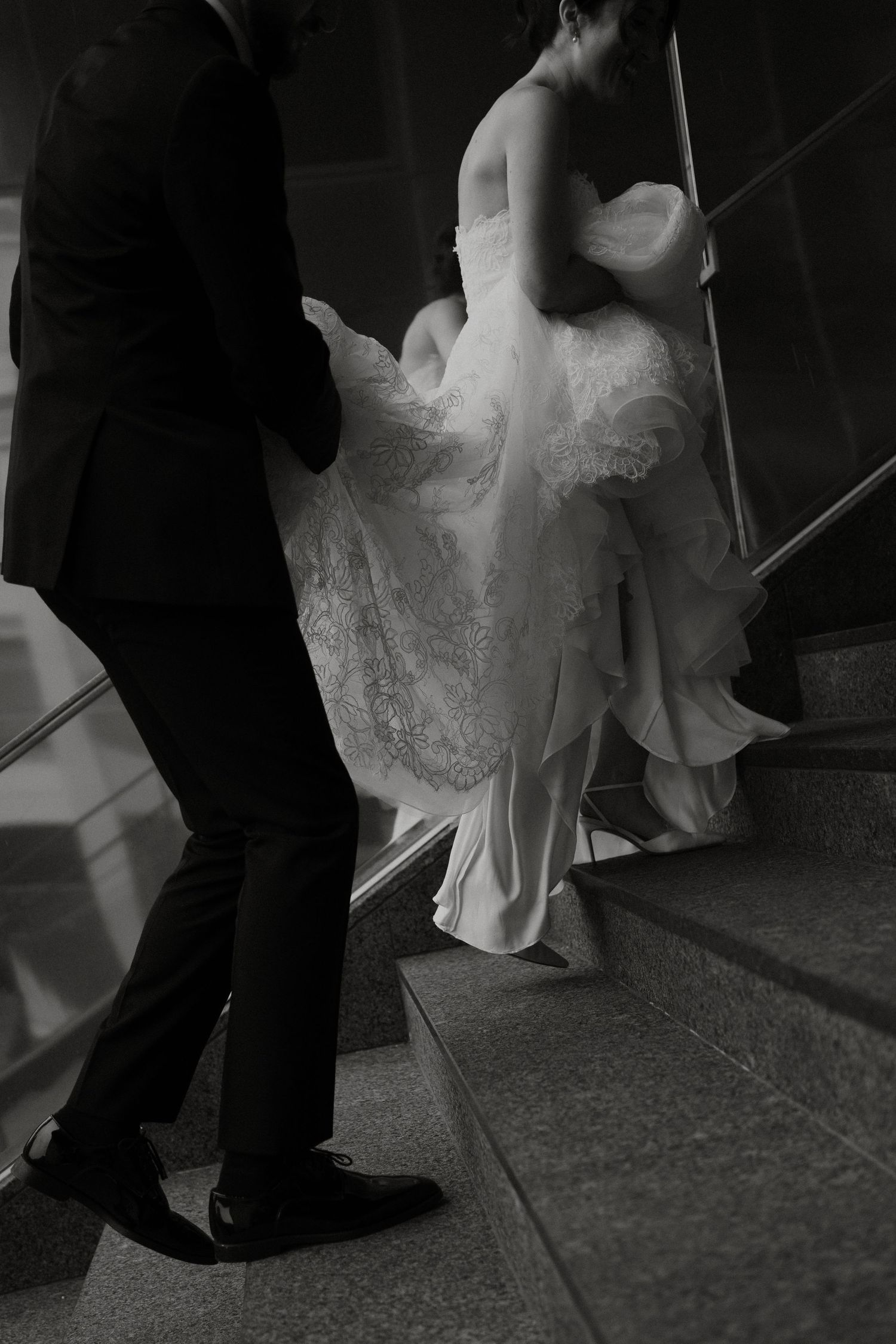 Black and white photo of bride and groom ascending stone staircase together.