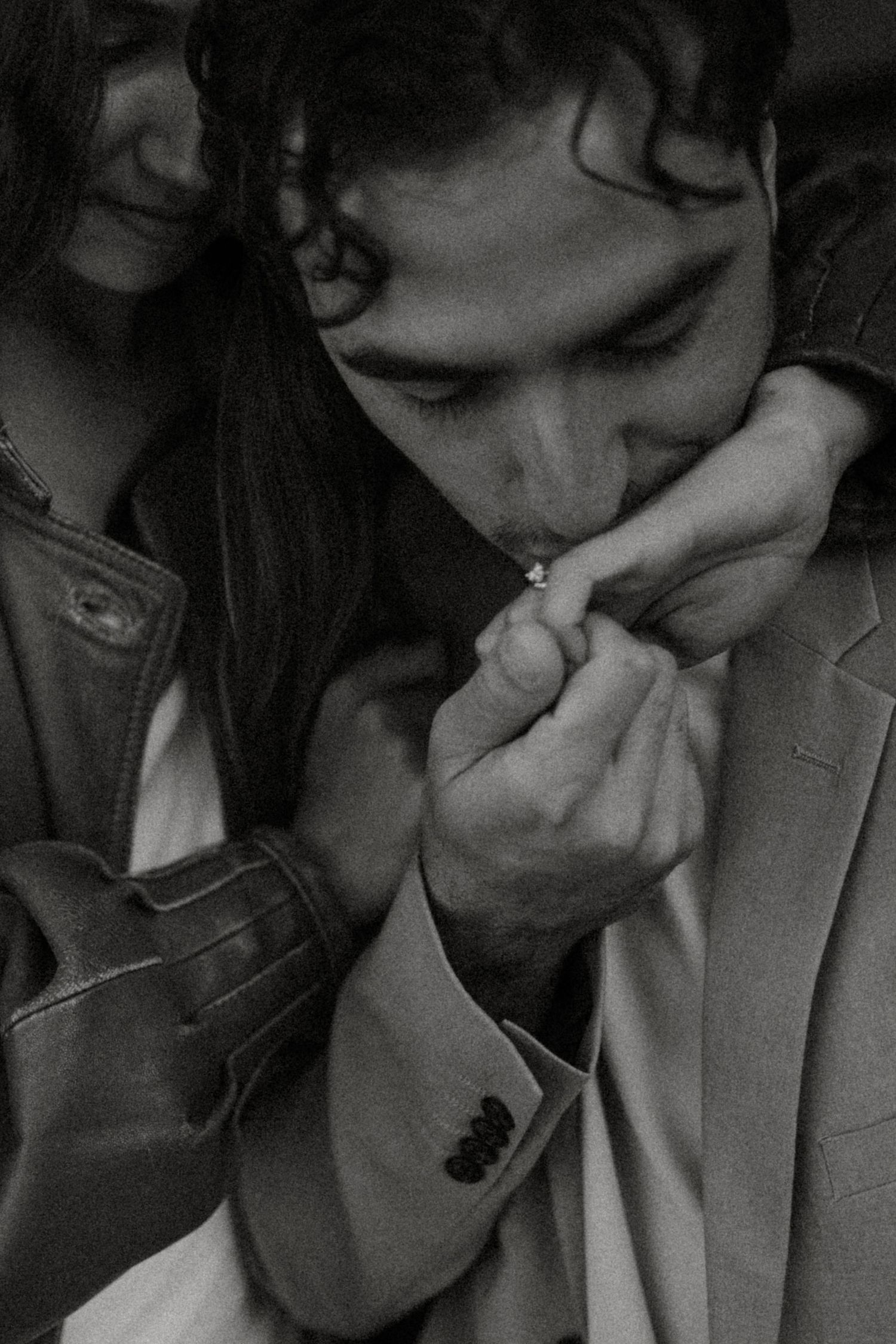 Black and white photo of a man in a suit kissing a woman's hand with a ring, as she smiles softly beside him.