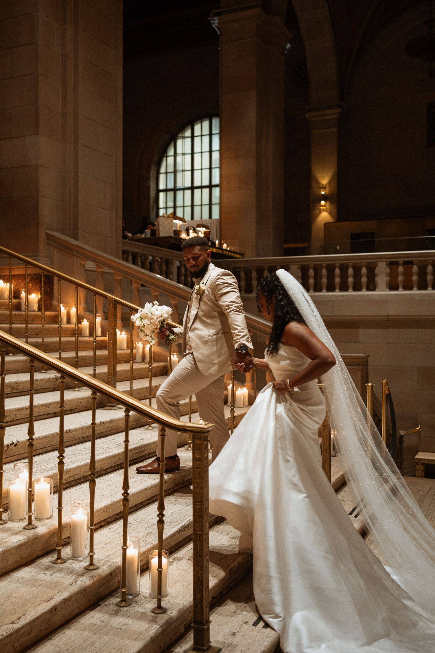 Bride and groom ascending candlelit staircase in a grand stone building, bride in flowing veil.
