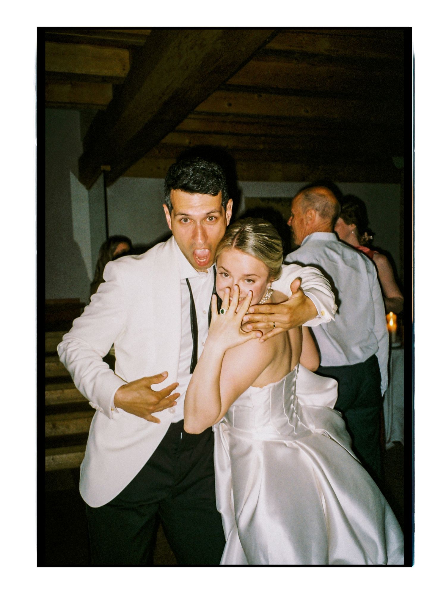 Bride and groom making fun expressions at wedding reception in rustic venue with wooden beams.