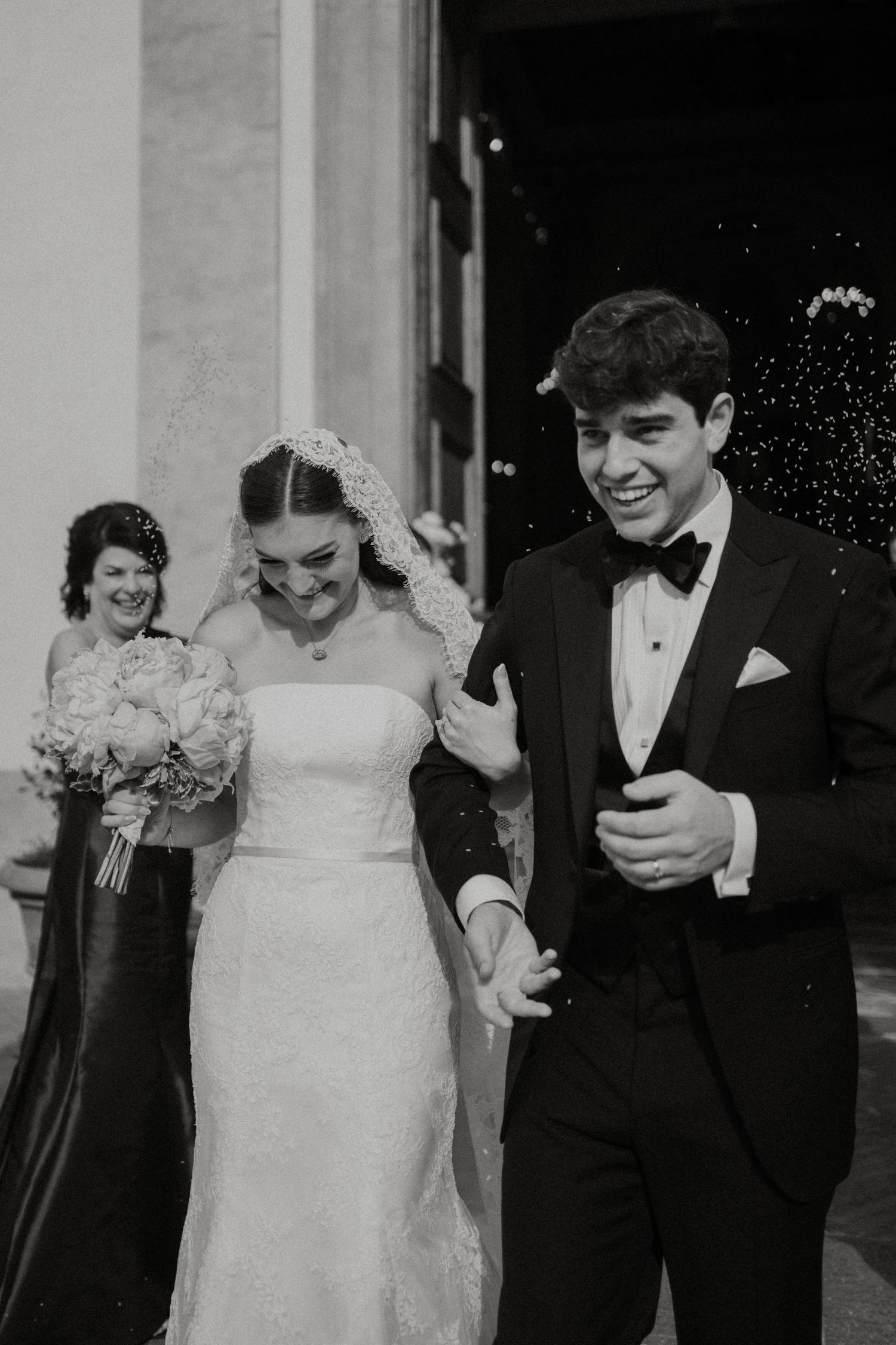 Black and white photo of smiling groom leading bride out of church after ceremony.
